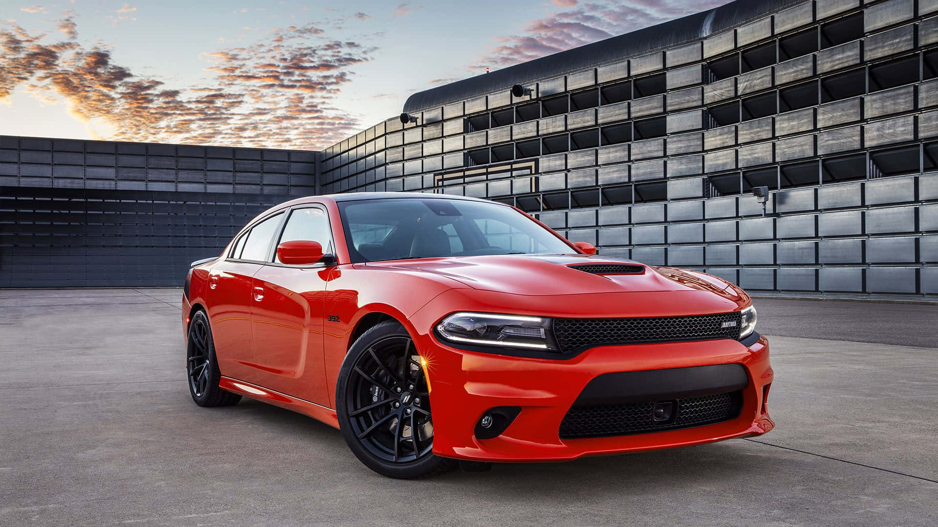 Dodge Charger 桌布 壁紙 — 一輛鮮紅色的道奇Charger停在一棟現代金屬建築前，背景是色彩繽紛的日落。