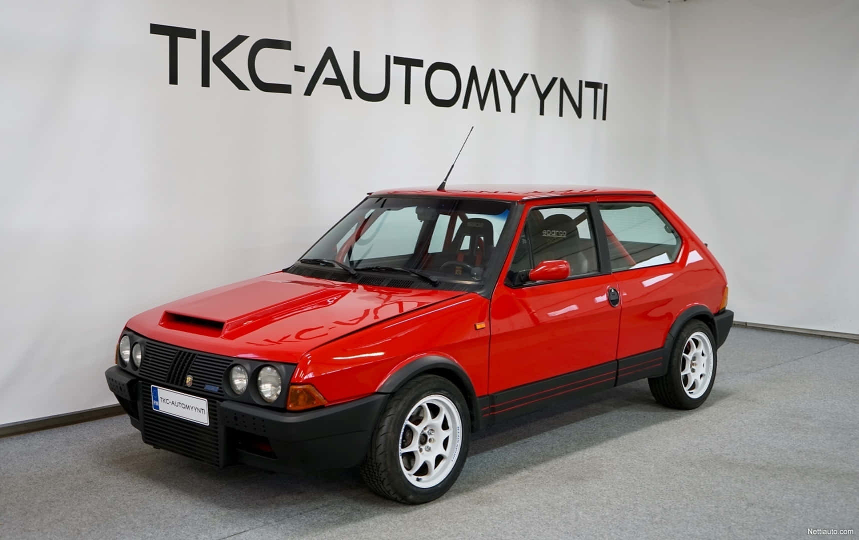 Fiat Ritmo 桌布 壁紙 — 一輛鮮紅色經典掀背車配白色車輪，在室內白色牆壁前展示，牆上有黑色文字。