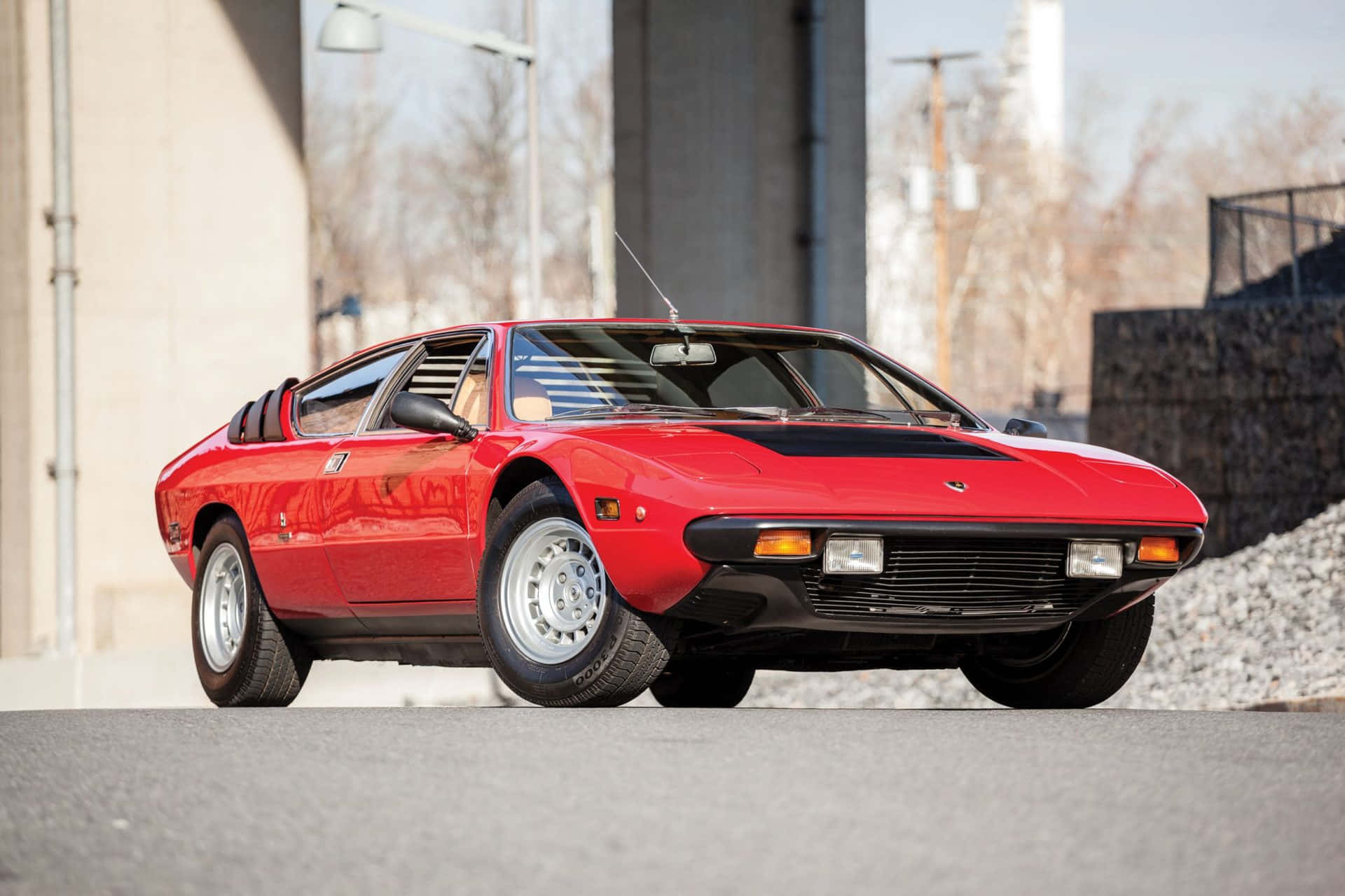 Lamborghini Urraco 桌布 壁紙 — 一輛鮮紅色經典跑車帶有黑色點綴，在晴朗日光下停泊在工業建築附近的瀝青路面上。