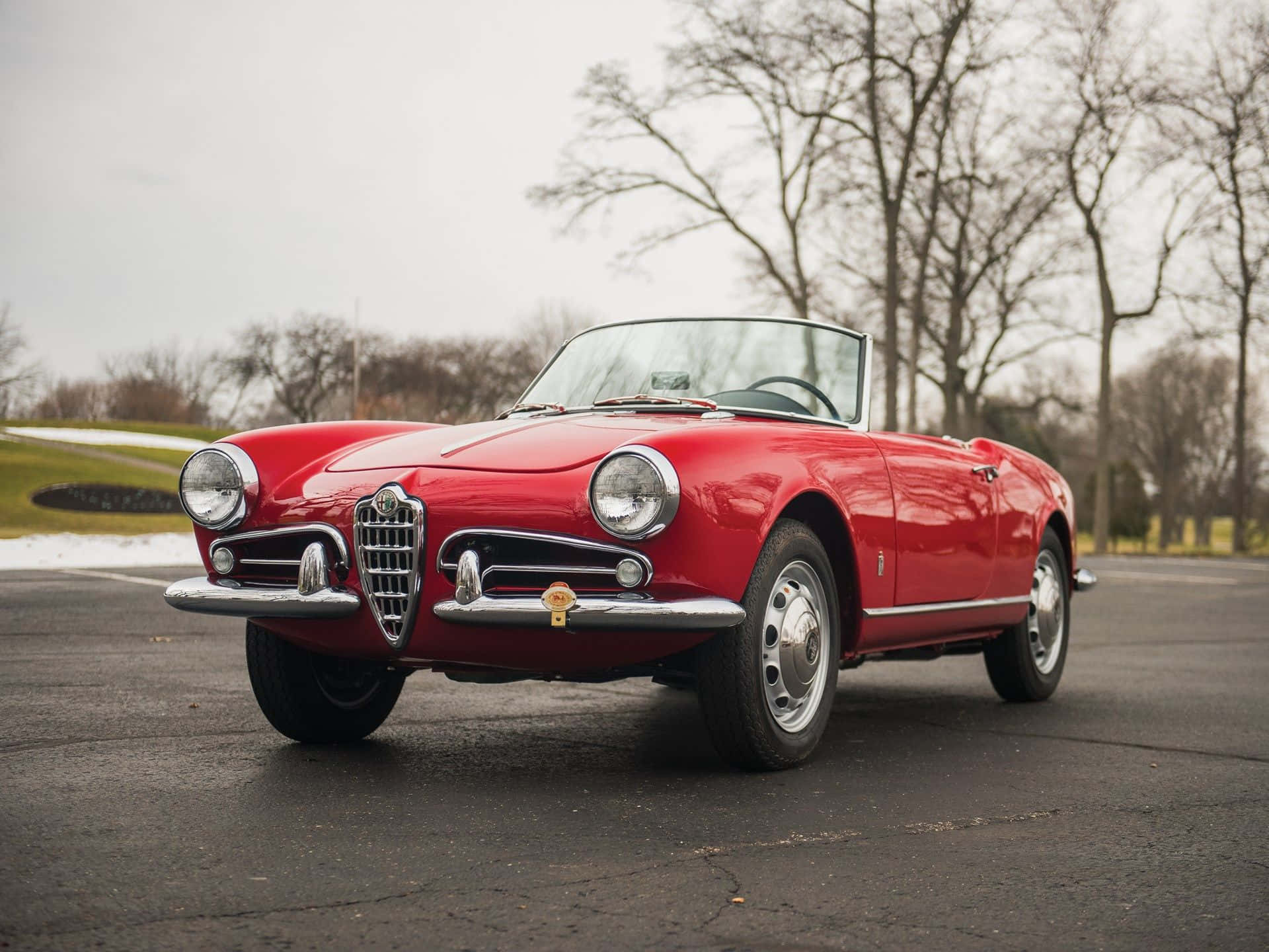Alfa Romeo Spider 桌布 壁紙 — 一輛鮮紅色經典阿爾法羅密歐Spider開篷車停在瀝青路上，背景有光禿禿的樹木和雪堆。