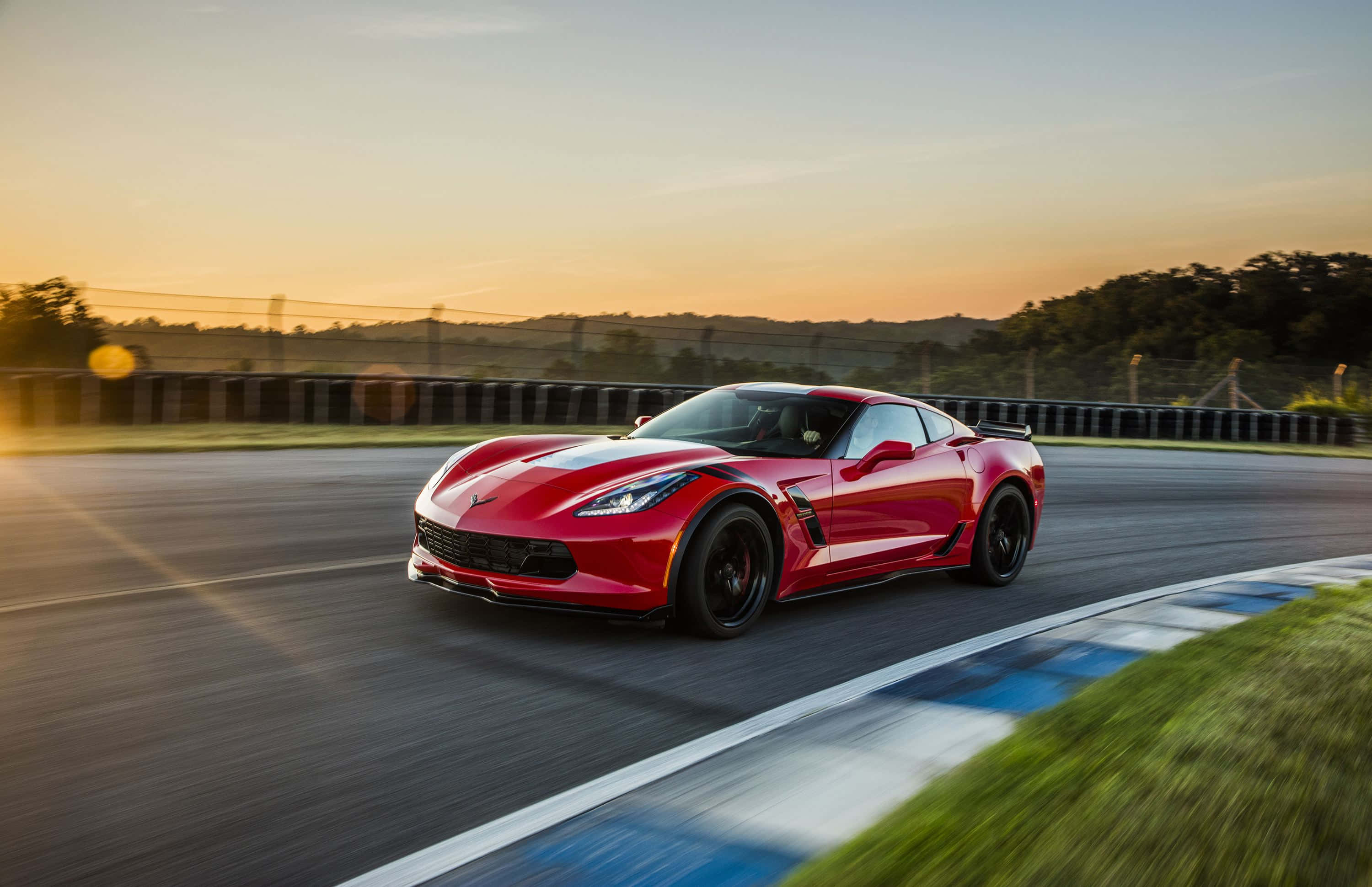 corvette 桌布 壁紙 — 一輛鮮紅色跑車在日落時分沿著賽道飛馳，帶有模糊的動態和溫暖的金色光芒。