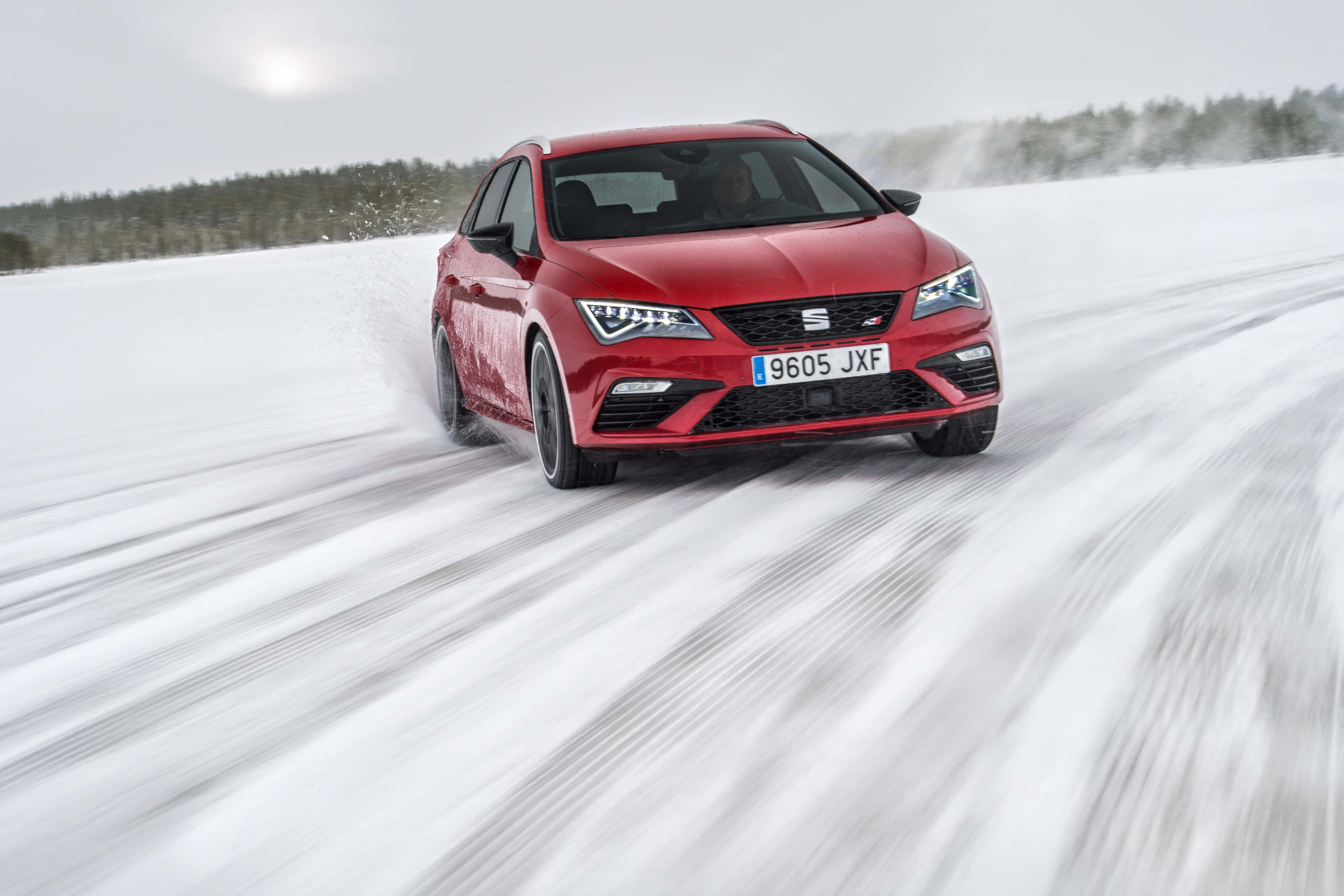 seat 桌布 壁紙 — 一輛鮮紅色跑車在雪地景觀中疾馳，揚起雪花，映襯著灰色的冬日天空。