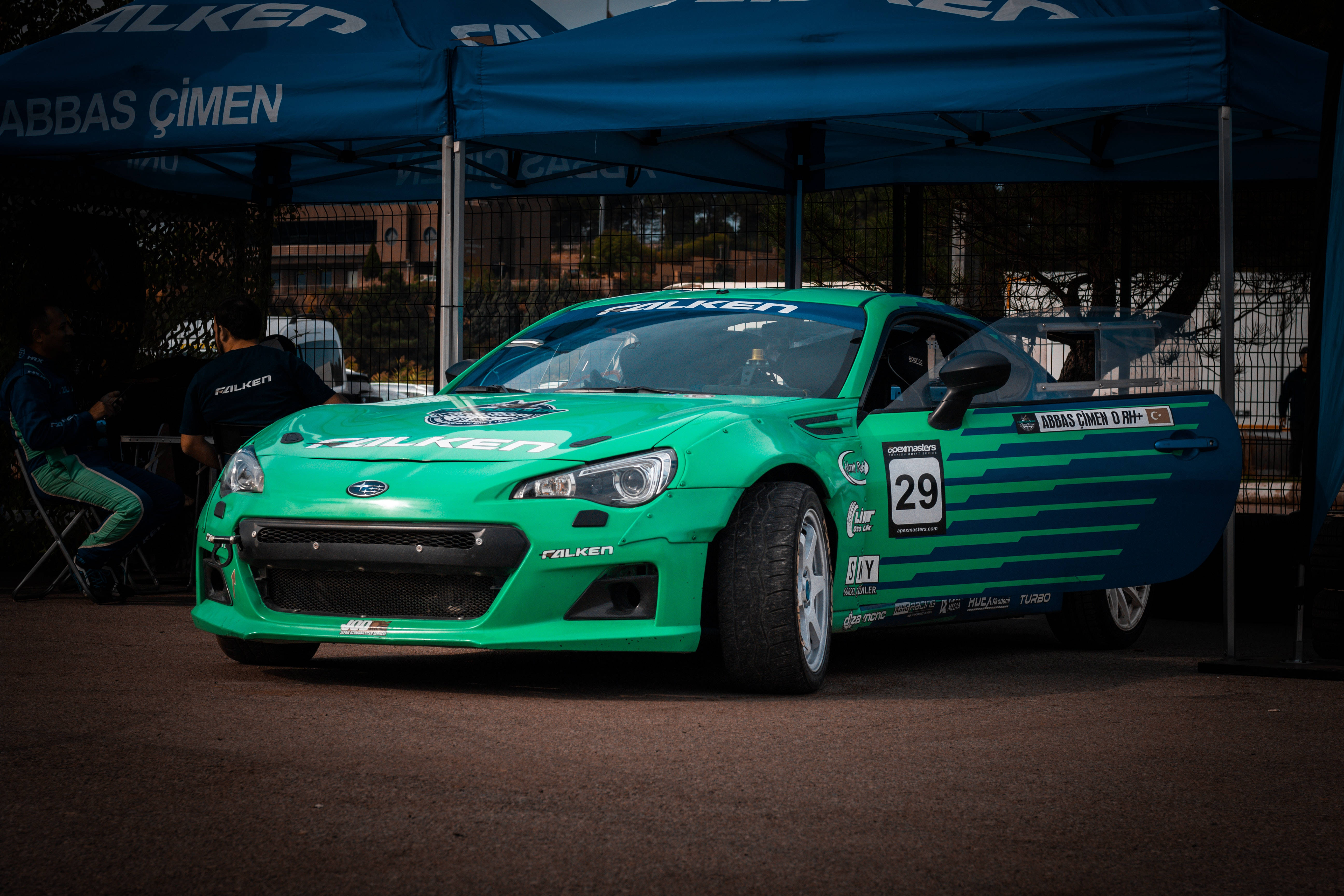 Sports Car 桌布 壁紙 — 一輛鮮綠色賽車（編號29）停泊在賽車活動的藍色簷篷下。