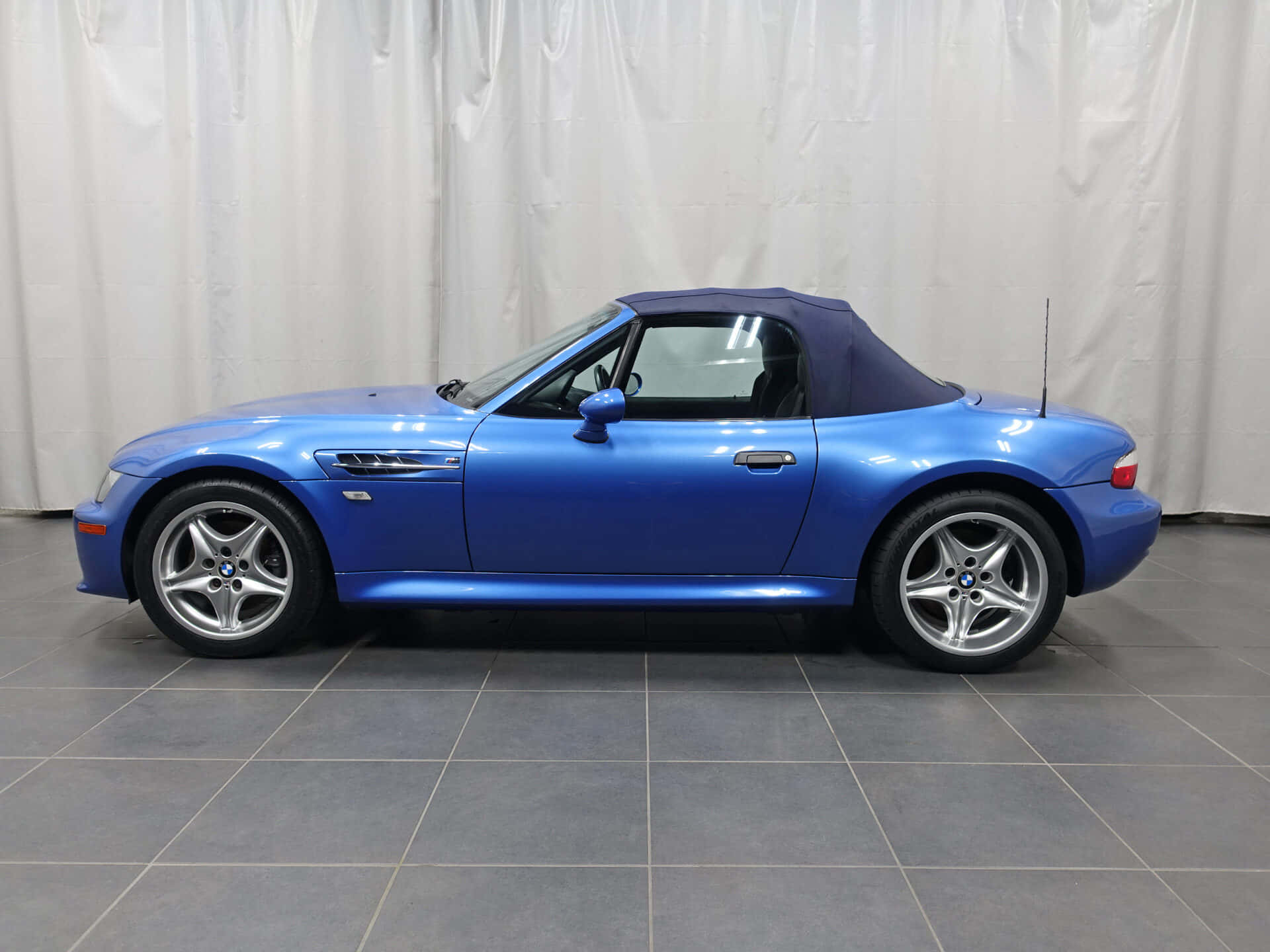 Bmw Z3 桌布 壁紙 — 一輛鮮藍色BMW Z8開篷跑車，配深藍色軟頂，停泊在灰色瓷磚地板上，背景為白色窗簾。