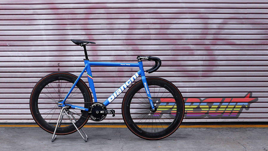 桌布 壁紙 — 一輛鮮藍色的Bianchi公路單車用腳架撐著，停靠在一個佈滿塗鴉、帶有醒目彩虹字母的金屬捲簾前。