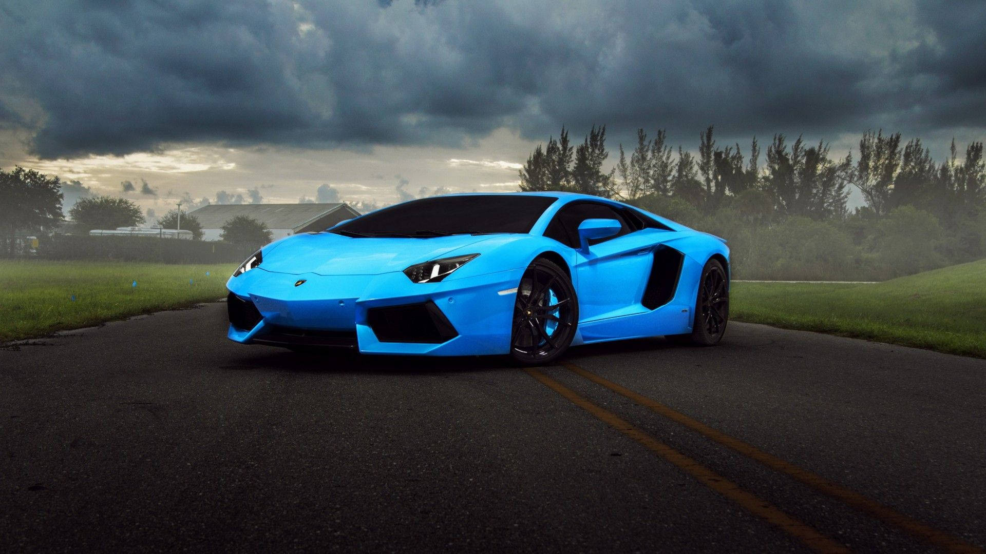 汽車 桌布 壁紙 — 一輛鮮藍色的林寶堅尼Aventador停在濕滑的道路上，背景是戲劇性的暴風雲、綠草和樹木。