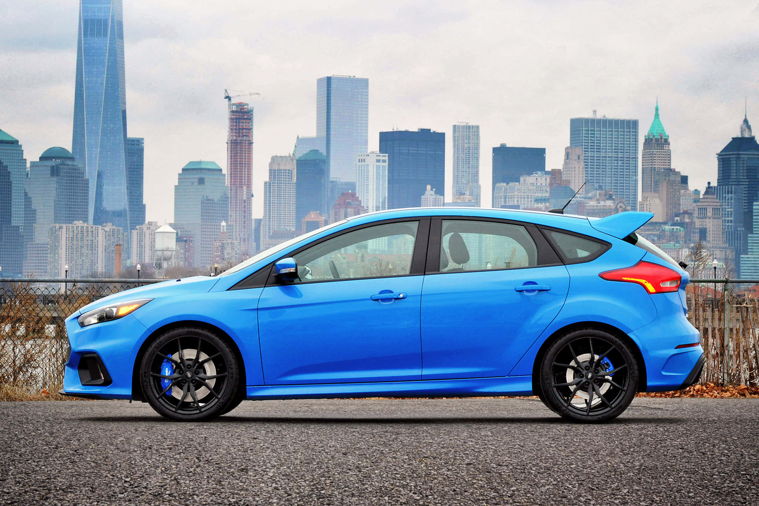 Ford Focus 桌布 壁紙 — 一輛鮮藍色的福特福克斯ST停在碎石上，背景是模糊的紐約市天際線。