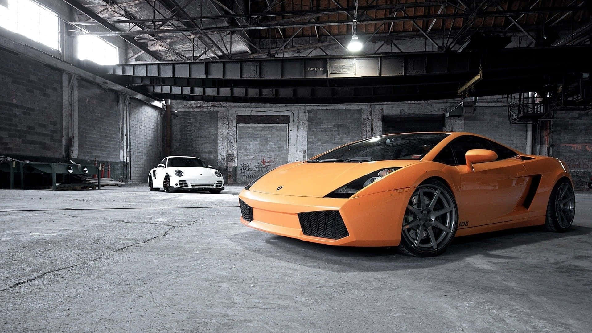 Garage 桌布 壁紙 — 一輛鮮豔的橙色林寶堅尼Gallardo和白色保時捷911停放在一個粗糙的工業倉庫內，有裸露的橫樑和混凝土地板。