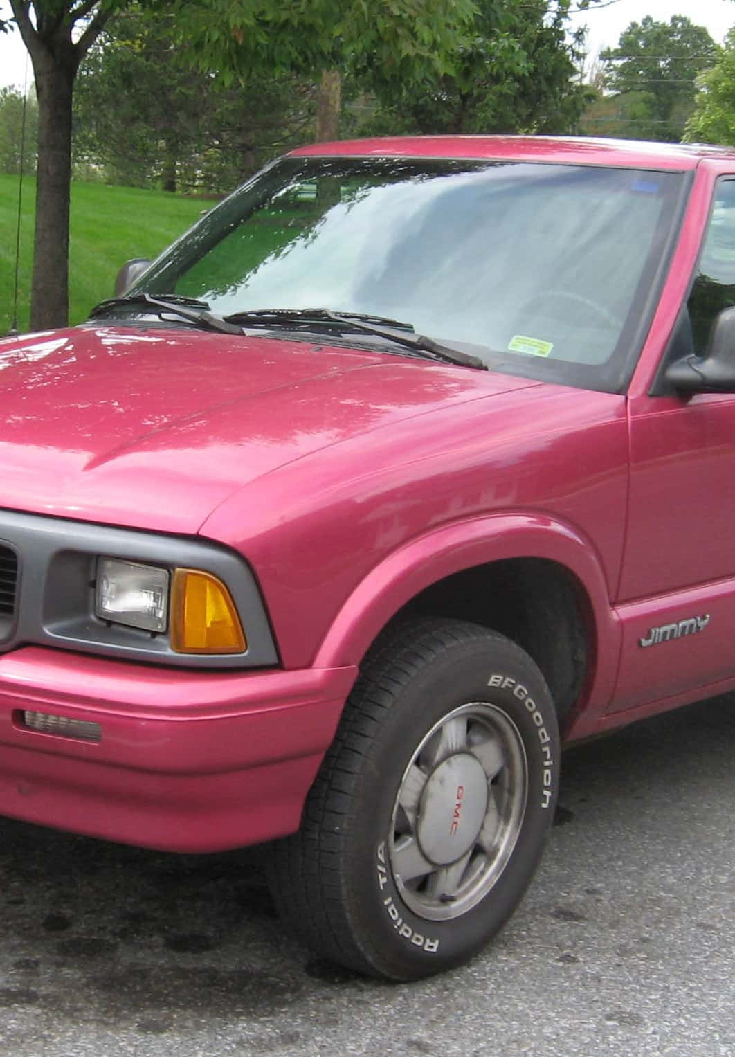 Gmc Jimmy 桌布 壁紙 — 一輛鮮豔的粉紅色GMC Jimmy SUV停泊在碎石上，背景有綠樹和草地。