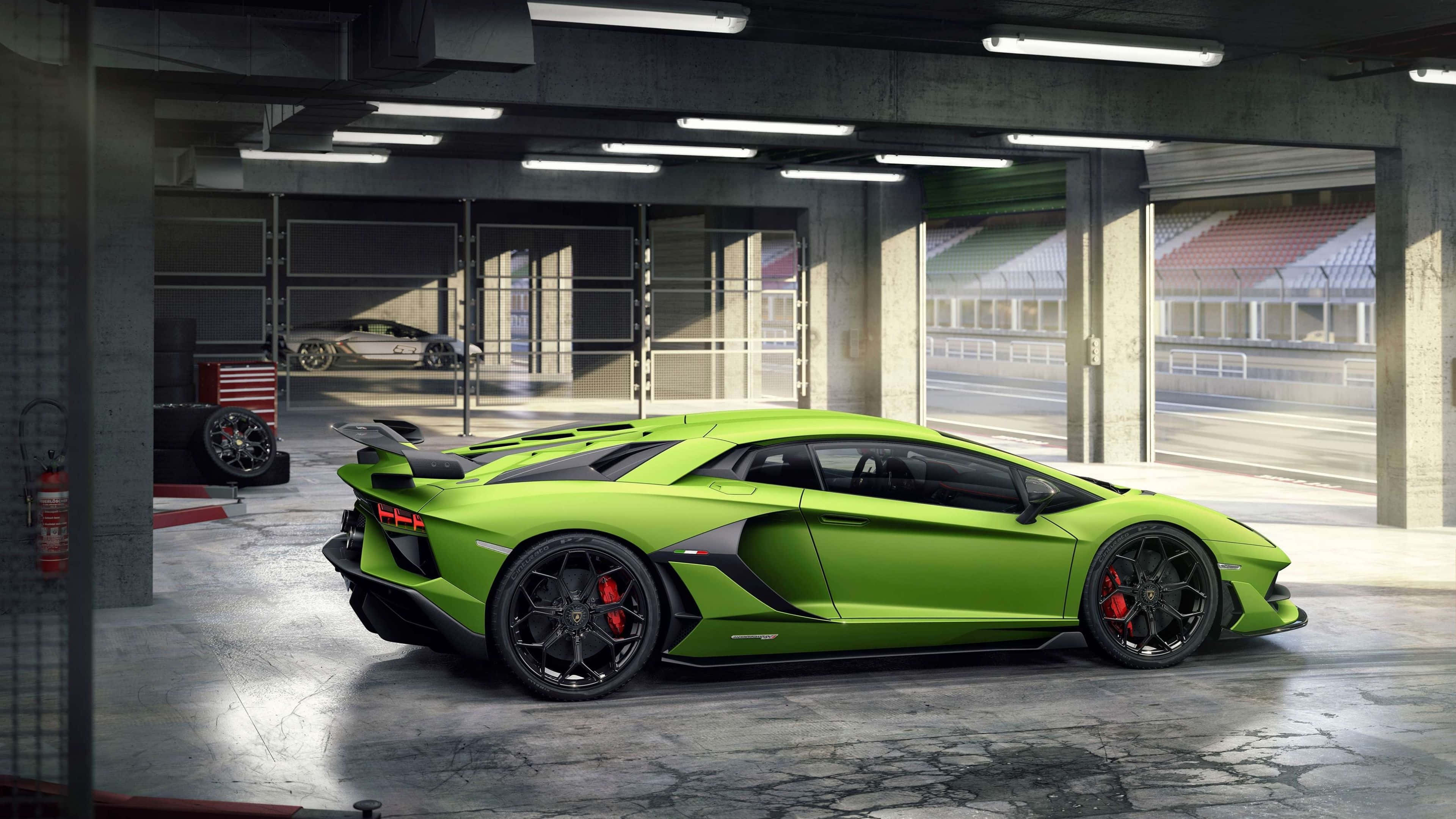林寶堅尼 4K 桌布 壁紙 — 一輛鮮豔的青檸綠色林寶堅尼Aventador SVJ停放在混凝土車庫中，透過敞開的車庫門可以看到賽道。