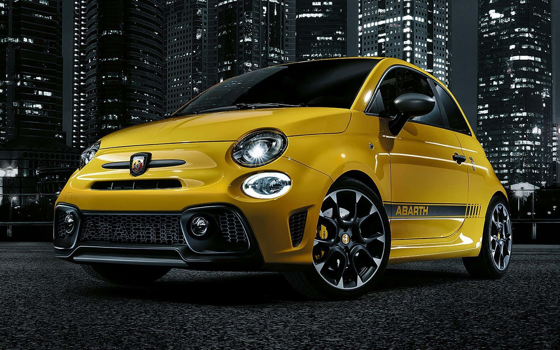 Abarth 桌布 壁紙 — 一輛鮮黃色的 Abarth Fiat 500 在夜晚高聳摩天大樓的背景下，於城市燈光下閃閃發光。