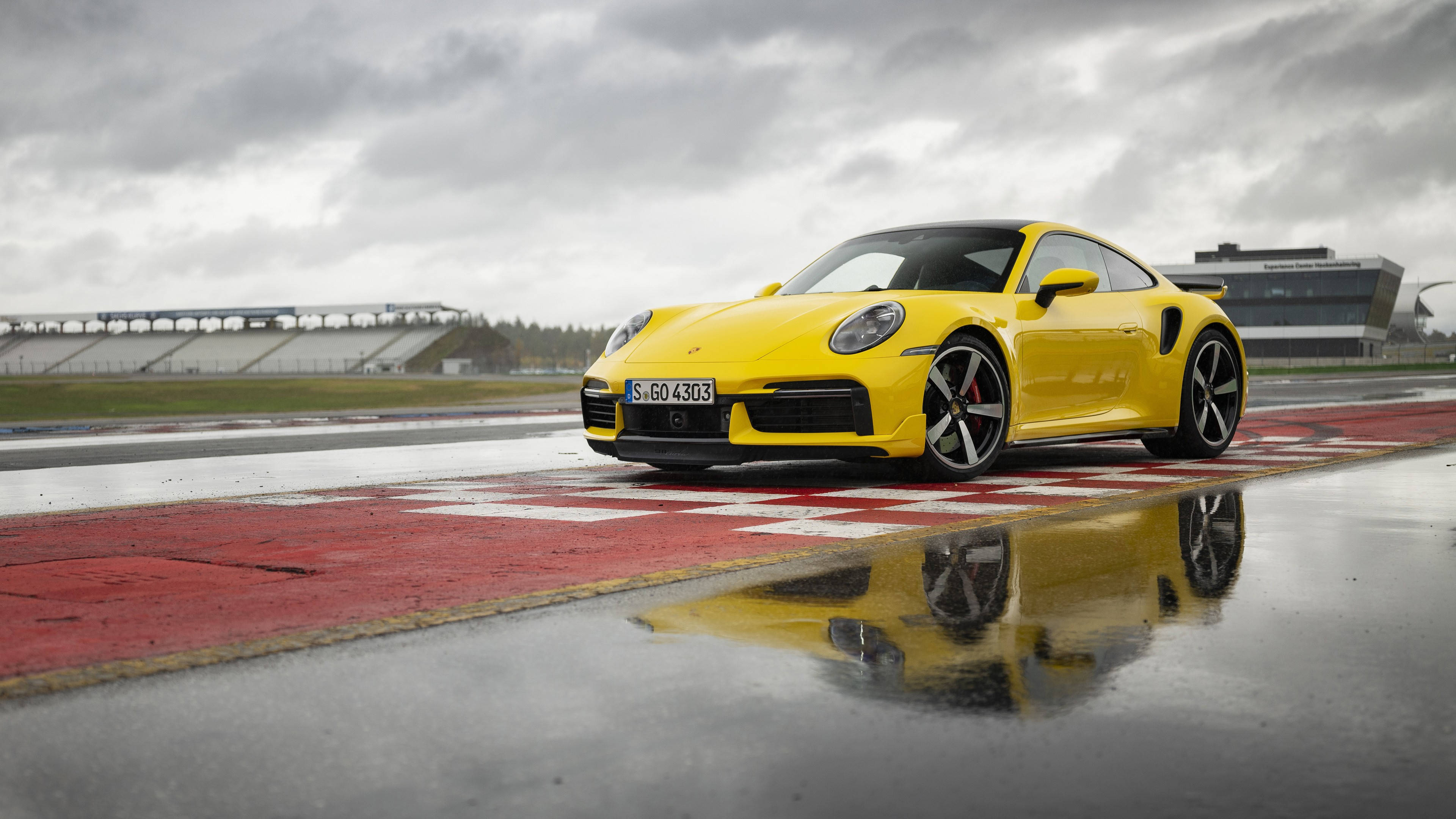 保時捷 桌布 壁紙 — 一輛鮮黃色的保時捷911 Turbo S停在潮濕的賽道上，其倒影在陰天下的水坑中閃爍。