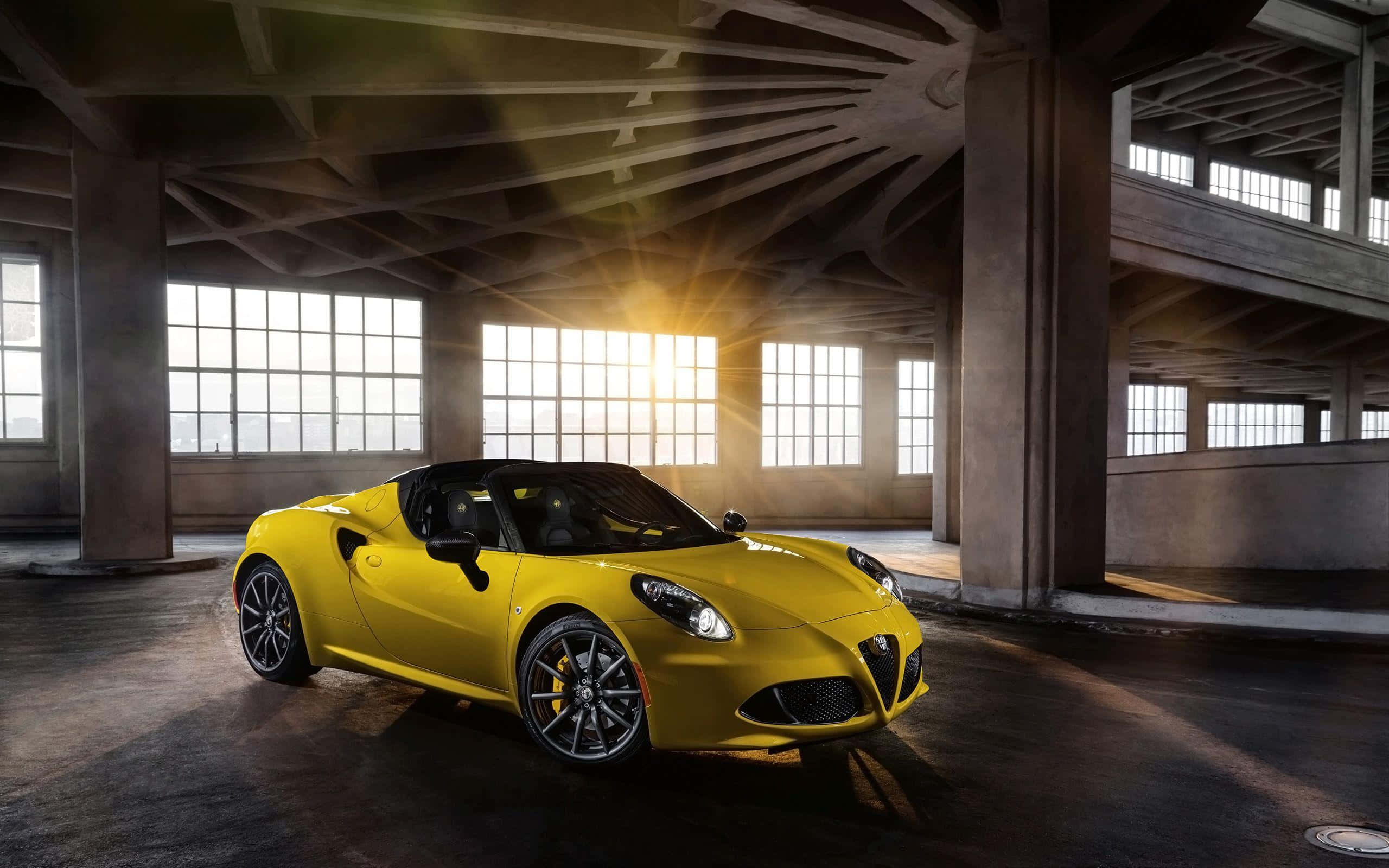 Alfa Romeo 4c 桌布 壁紙 — 一輛鮮黃色的愛快羅密歐Spider開篷車在金色夕陽下閃耀，陽光穿過破舊工業倉庫的大窗戶灑落。