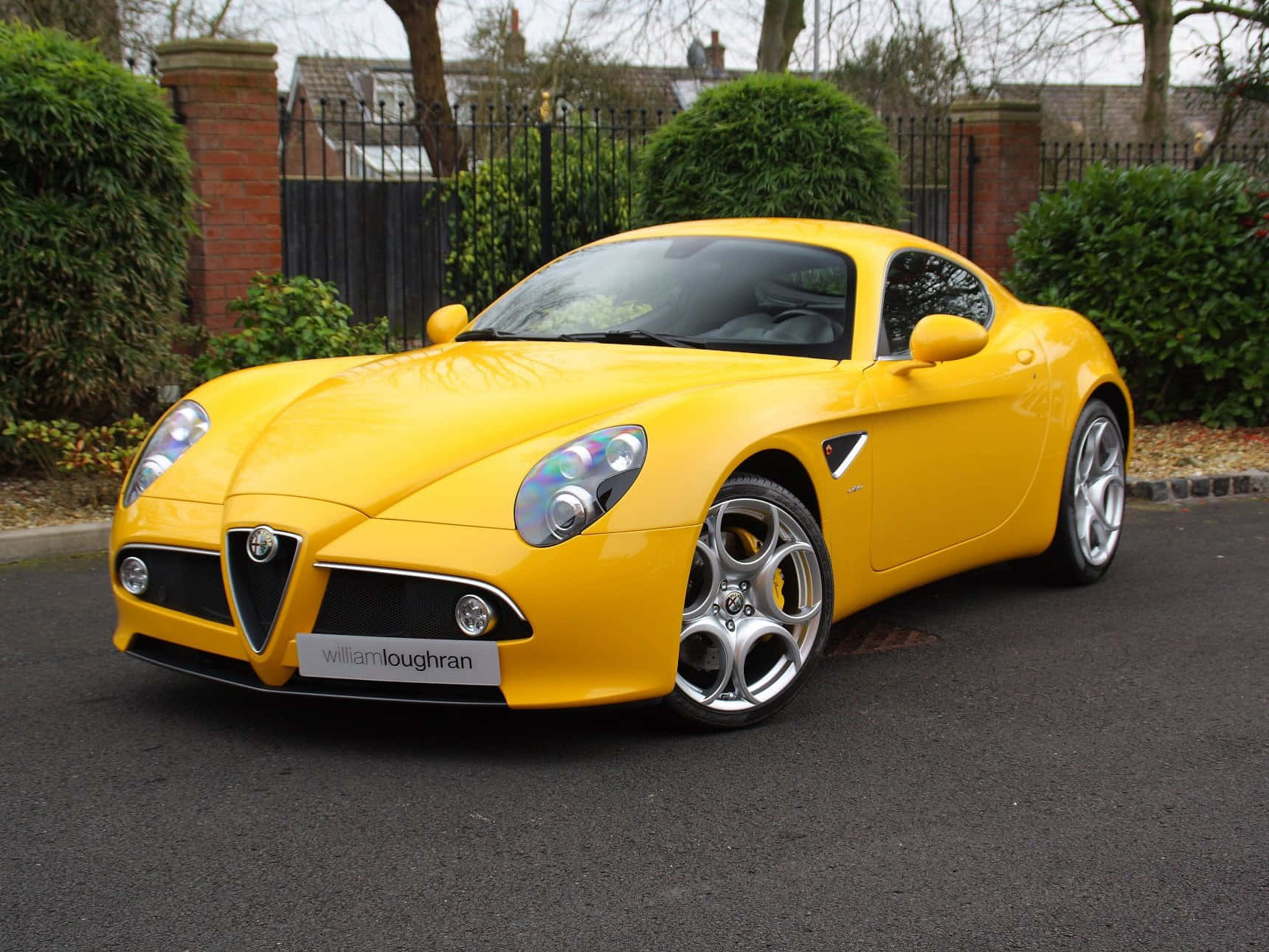 Alfa Romeo 8c Competizione 桌布 壁紙 — 一輛鮮黃色的愛快羅密歐跑車在陰天之下停泊在寧靜的住宅街道上閃閃發光。