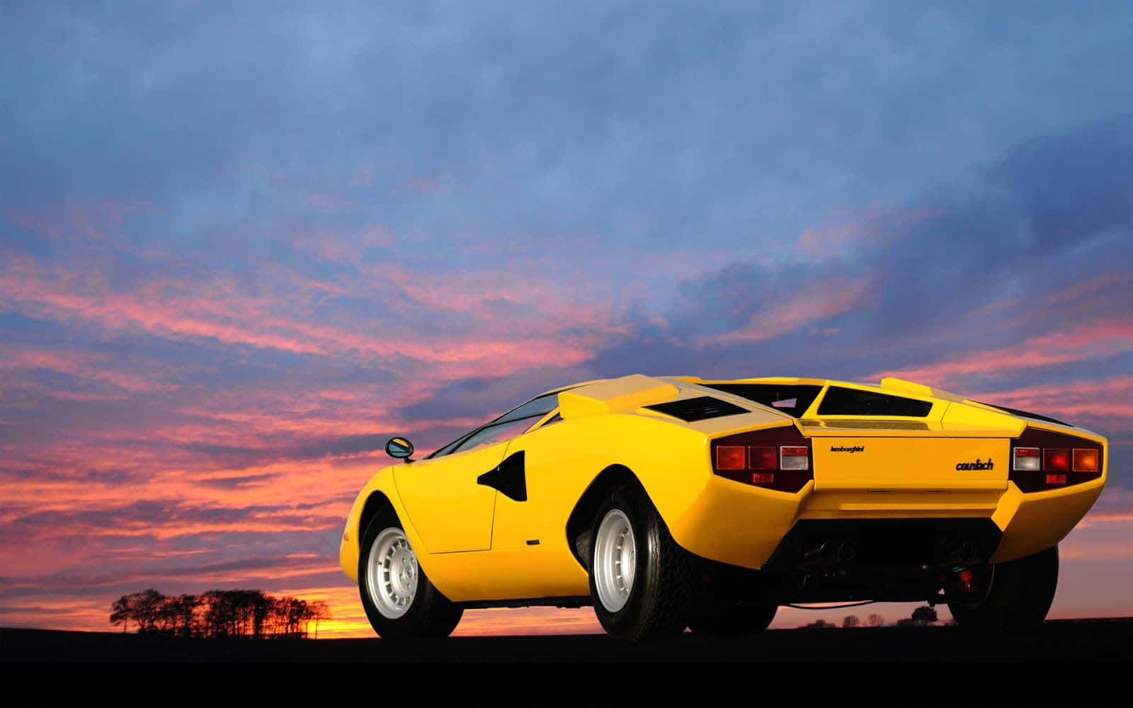 Lamborghini Countach 桌布 壁紙 — 一輛鮮黃色的林寶堅尼Countach停泊在日落時分的山丘上，上方有火熱的橙色和紫色雲彩。