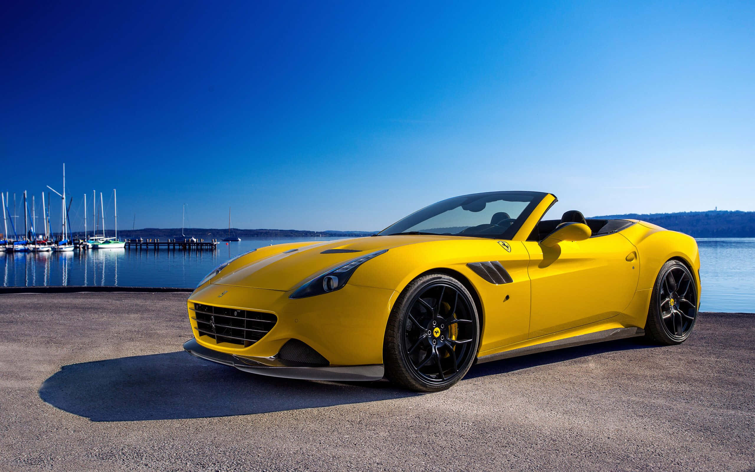 Ferrari California T 桌布 壁紙 — 一輛鮮黃色的法拉利開篷車停泊在碼頭上，背景有帆船和寧靜的水面，天空清澈湛藍。