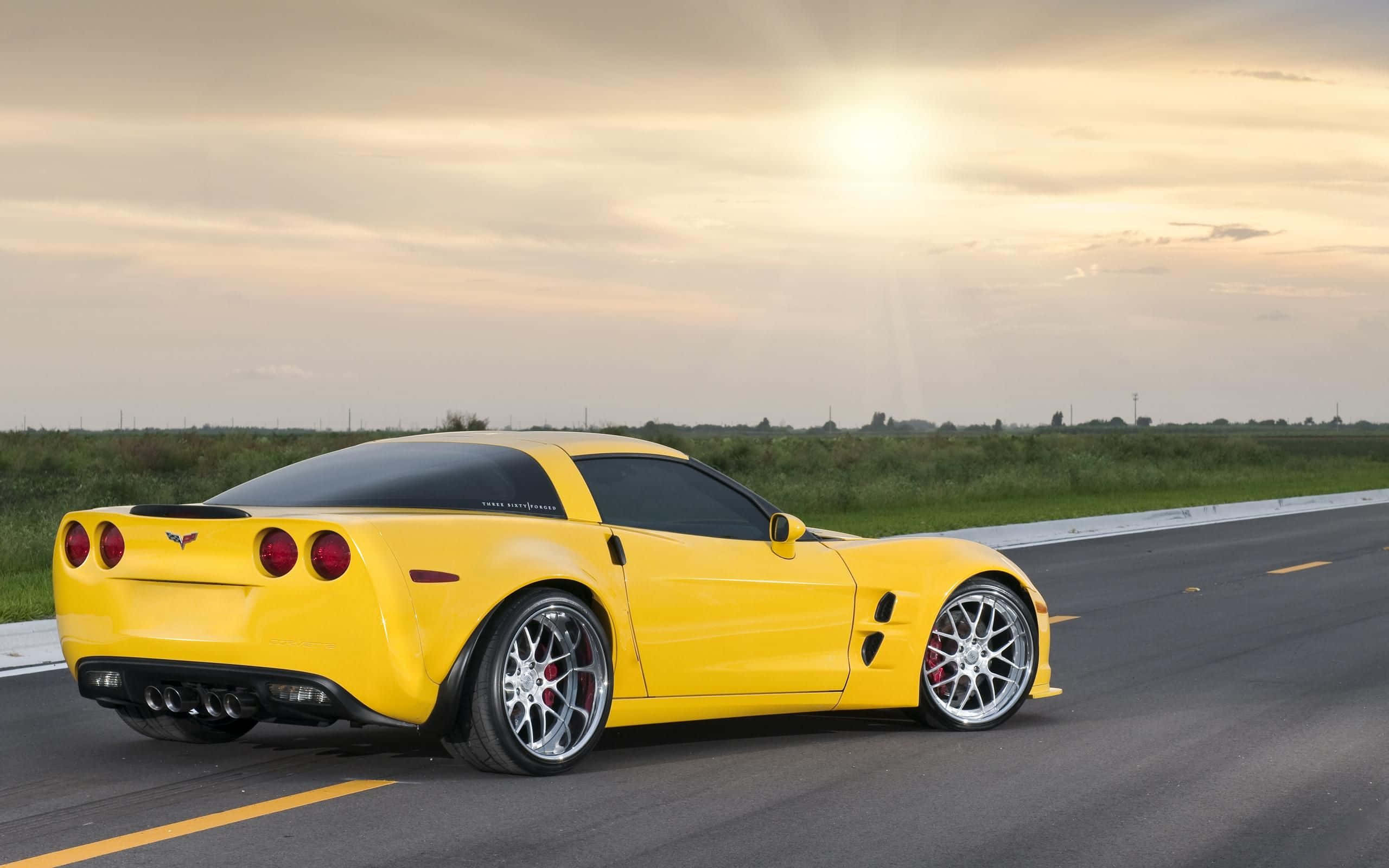 corvette 桌布 壁紙 — 一輛鮮黃色的雪佛蘭克爾維特跑車在日落時分行駛在高速公路上，金色的陽光投下長長的影子。