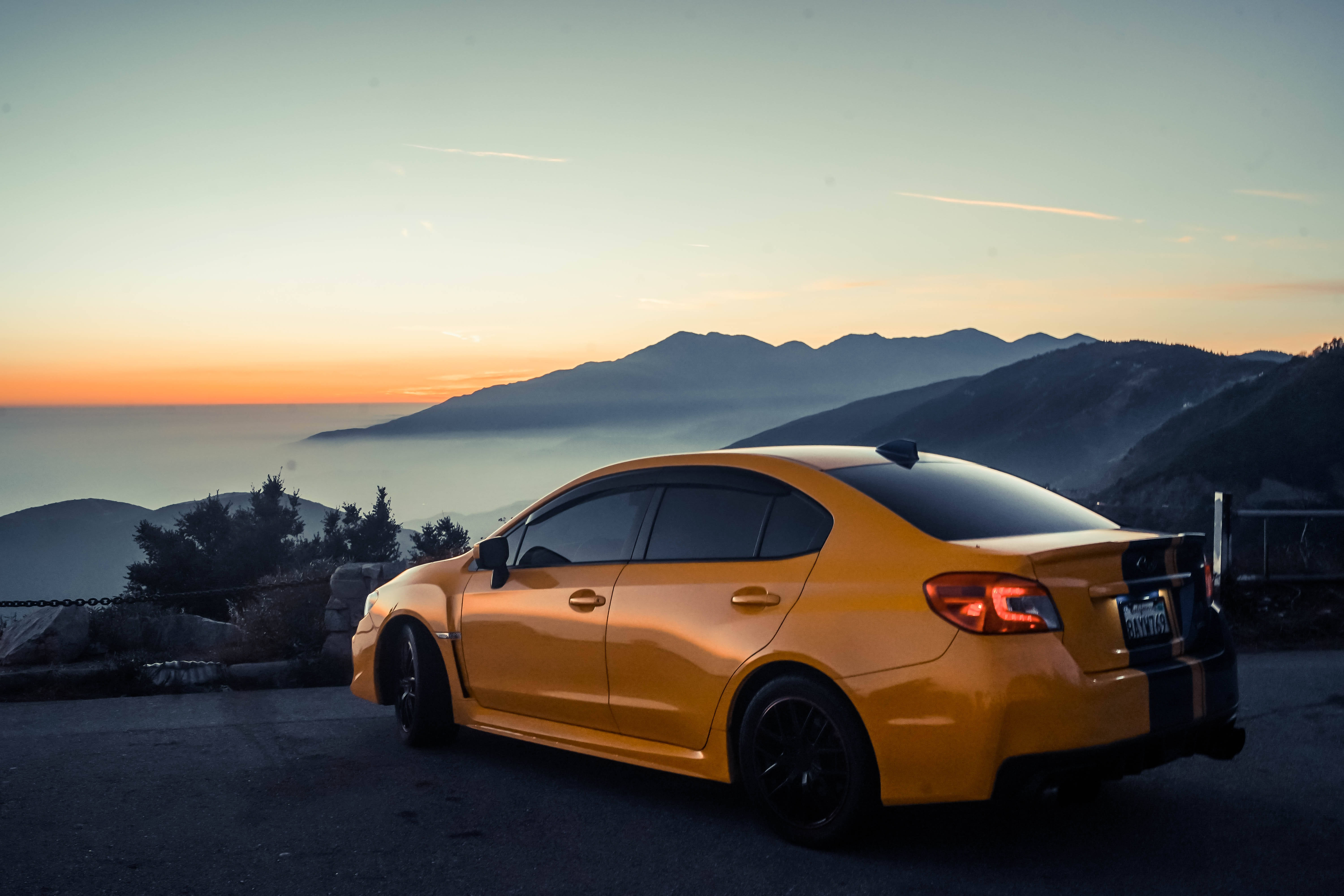 subaru 桌布 壁紙 — 一輛鮮黃色轎車停在山頂觀景點，夕陽西下，霧氣繚繞的山峰和下方的海洋盡收眼底。
