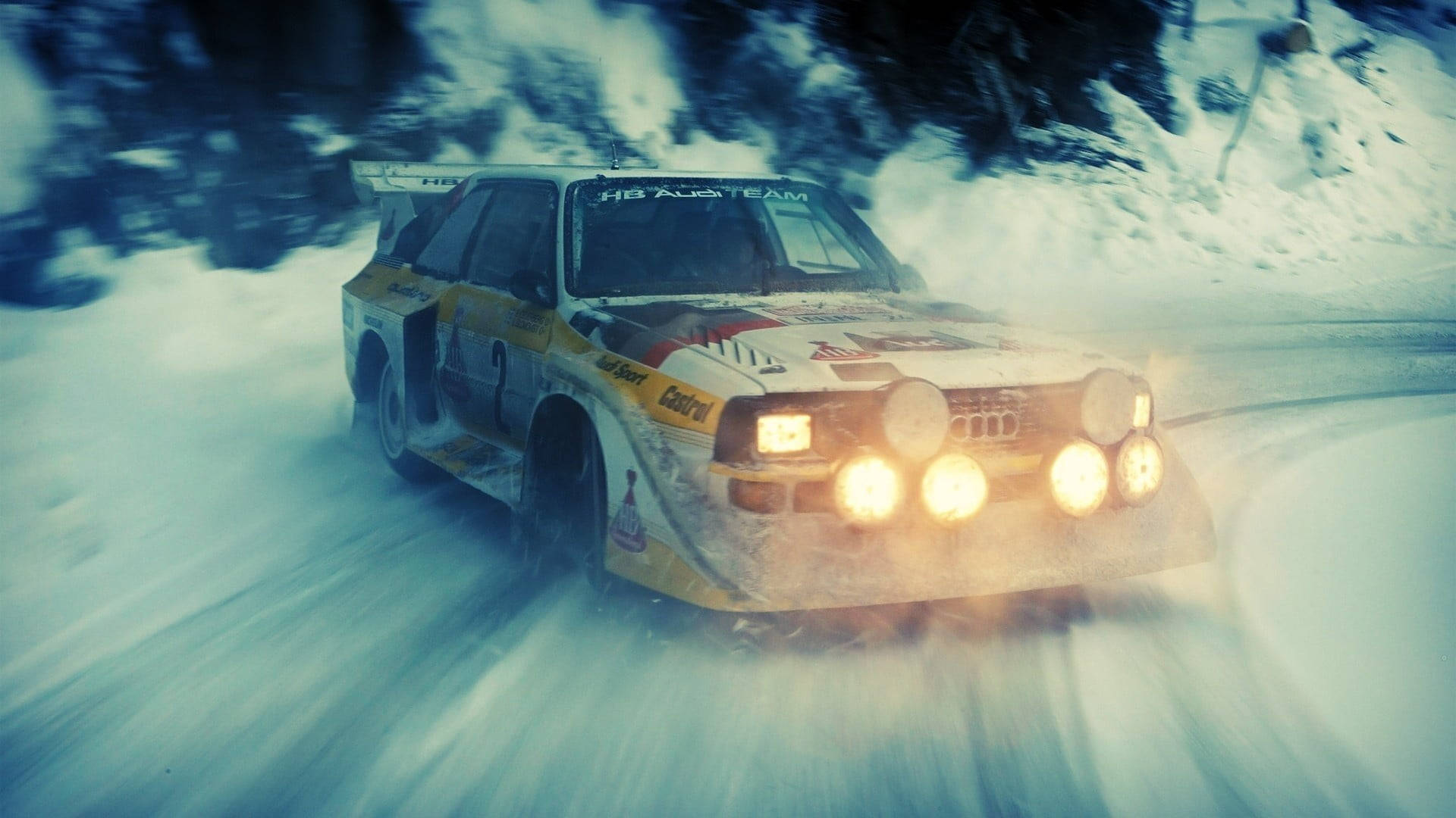 黃色拉力賽車在雪地森林中亮著車頭燈奔馳。 — 奧迪 GIF 壁紙