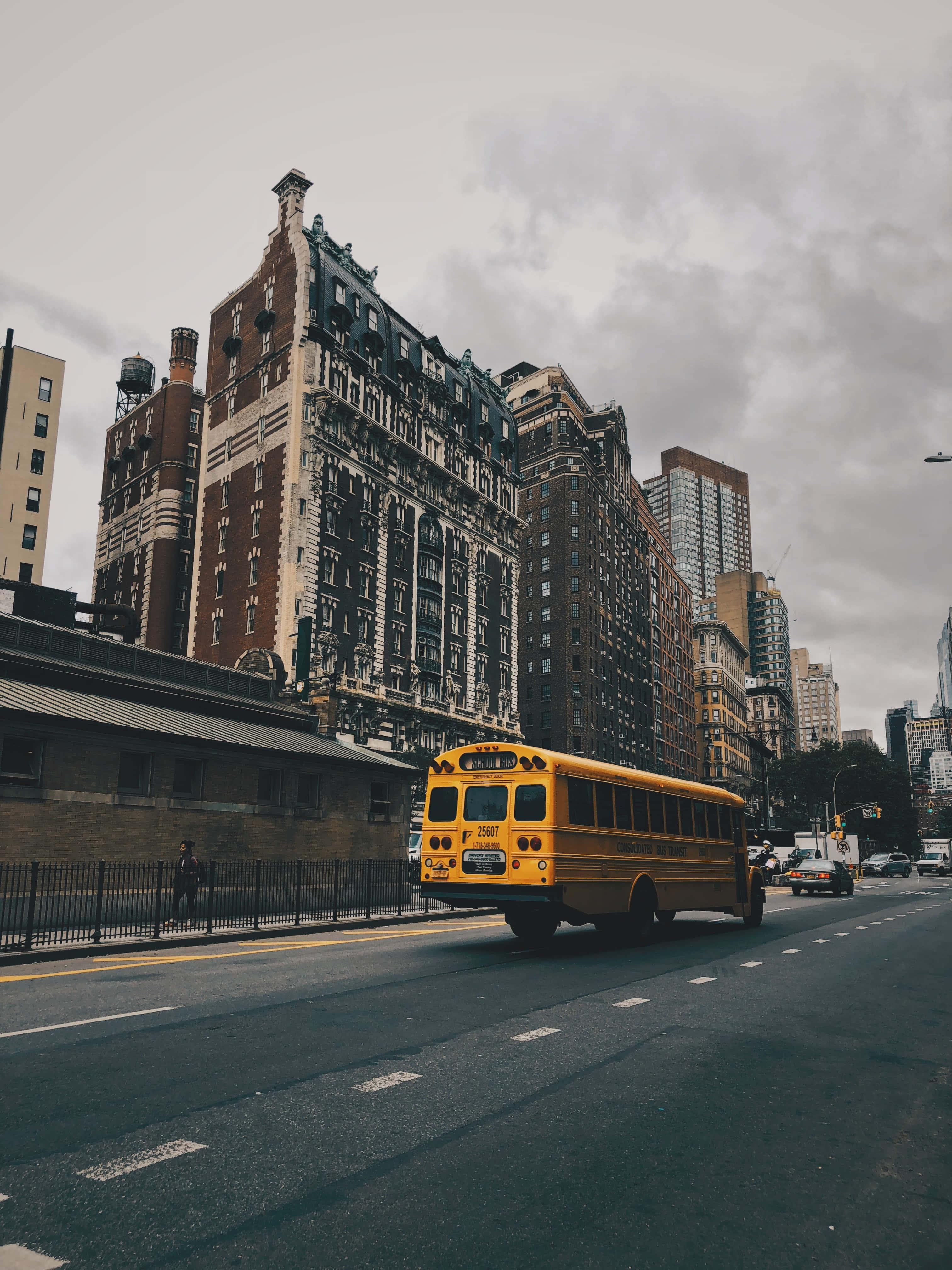 Yellow School Bus 桌布 壁紙 — 一輛黃色校車在潮濕的城市街道上行駛，經過裝飾華麗的褐石建築，天空多雲。