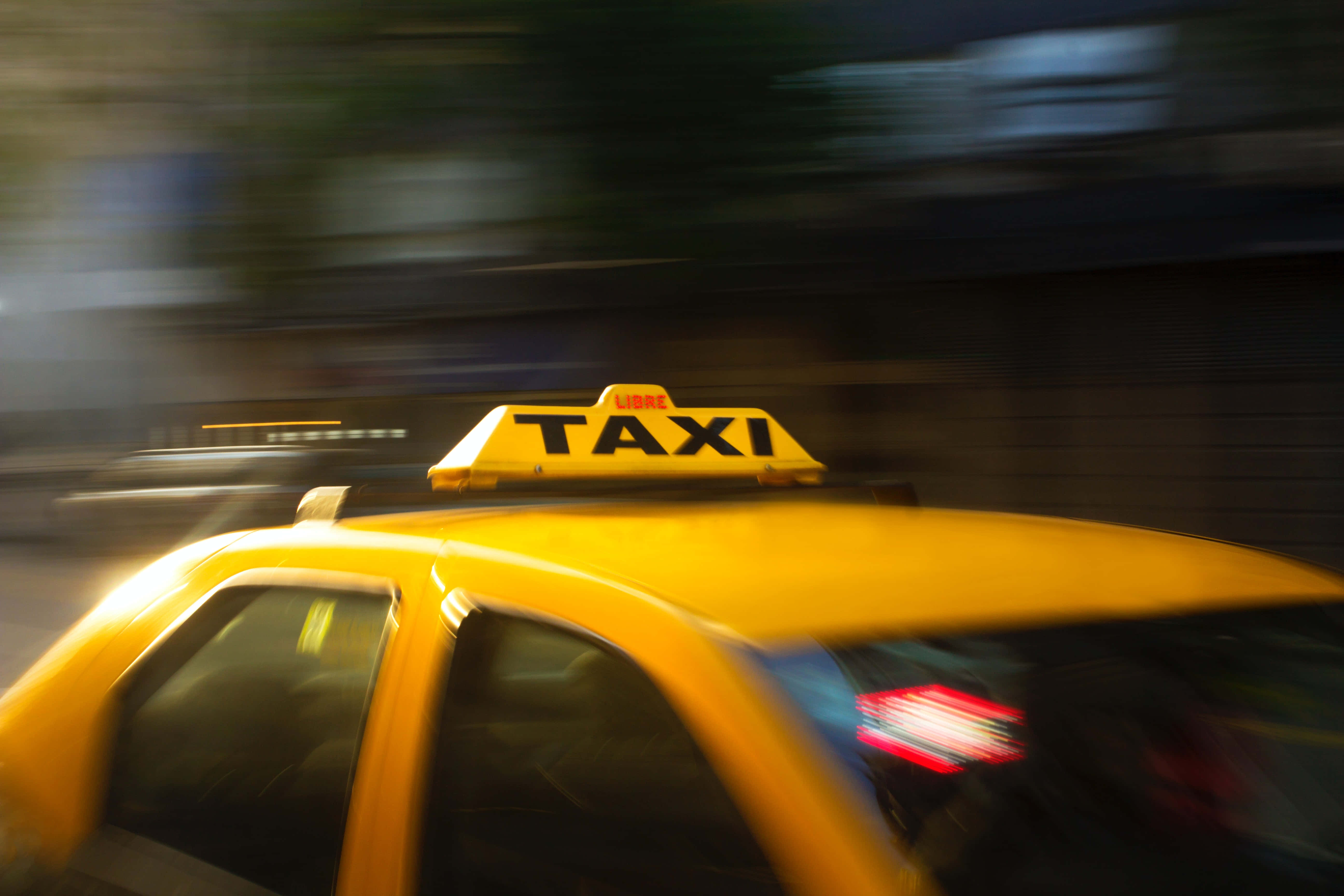 Yellow Cab 桌布 壁紙 — 一輛黃色的士在夜間穿過城市街道，帶有移動的霓虹燈條紋模糊效果。