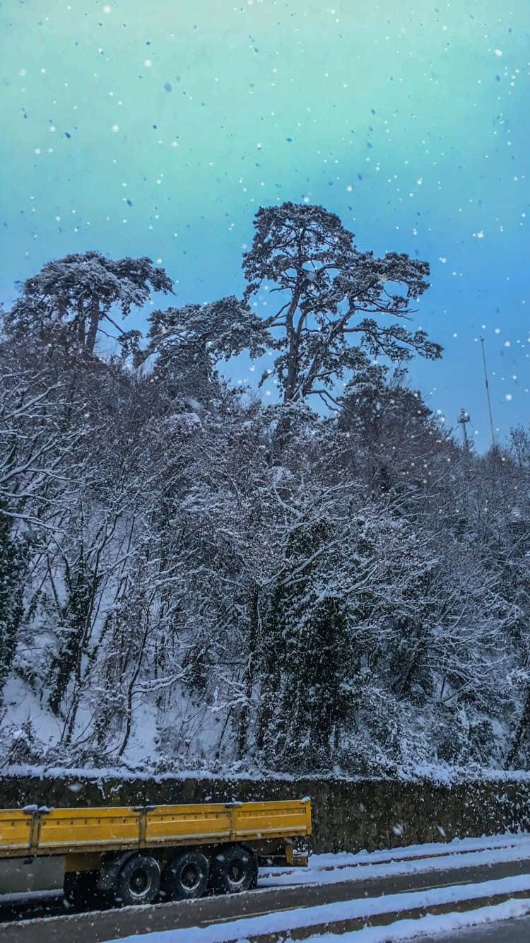 Winter Phone 桌布 壁紙 — 一輛黃色貨車在飄雪的暮色天空下行駛，經過積雪的樹木。
