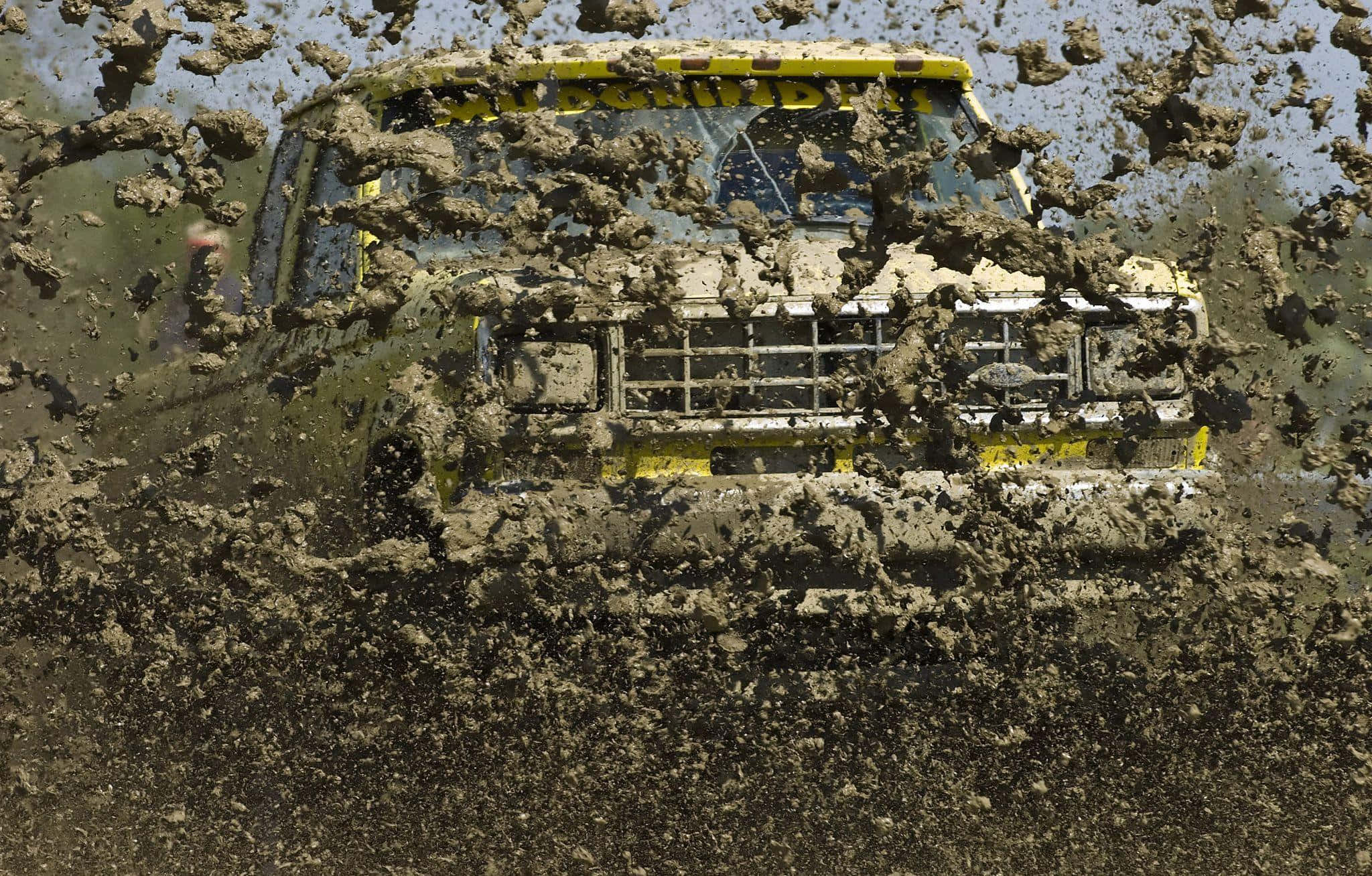 mud 桌布 壁紙 — 一輛黃色越野車衝破厚泥，在明亮的日光下以慢動作噴灑水滴。