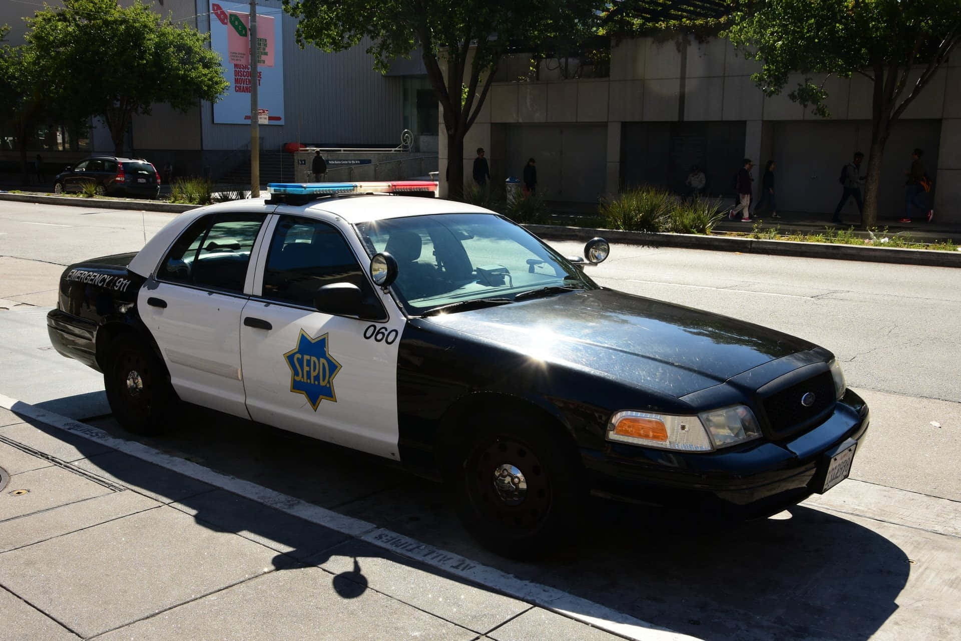 Ford Crown Victoria 桌布 壁紙 — 一輛黑白相間的SEPD警車停泊在陽光明媚的城市街道上，背景有樹木和行人。