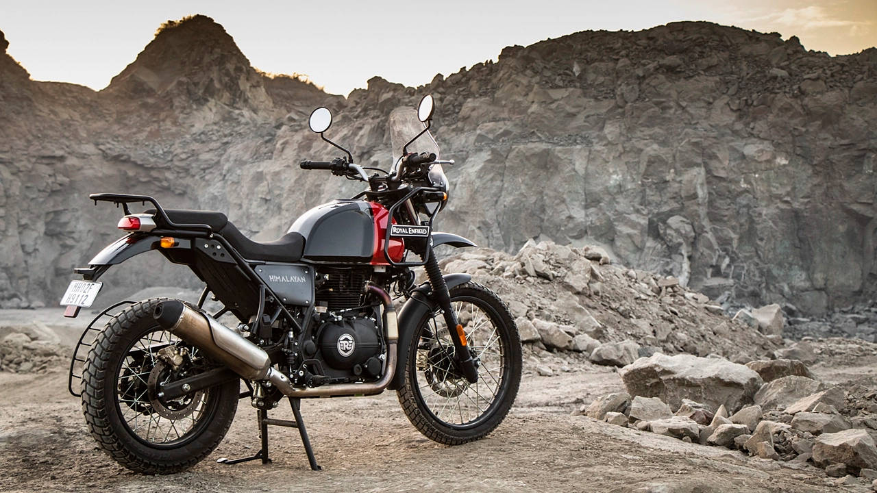 自行車 桌布 壁紙 — 一輛黑紅色的 Royal Enfield Himalayan 電單車在黃金時段矗立在崎嶇地形上，背景是岩石峭壁。