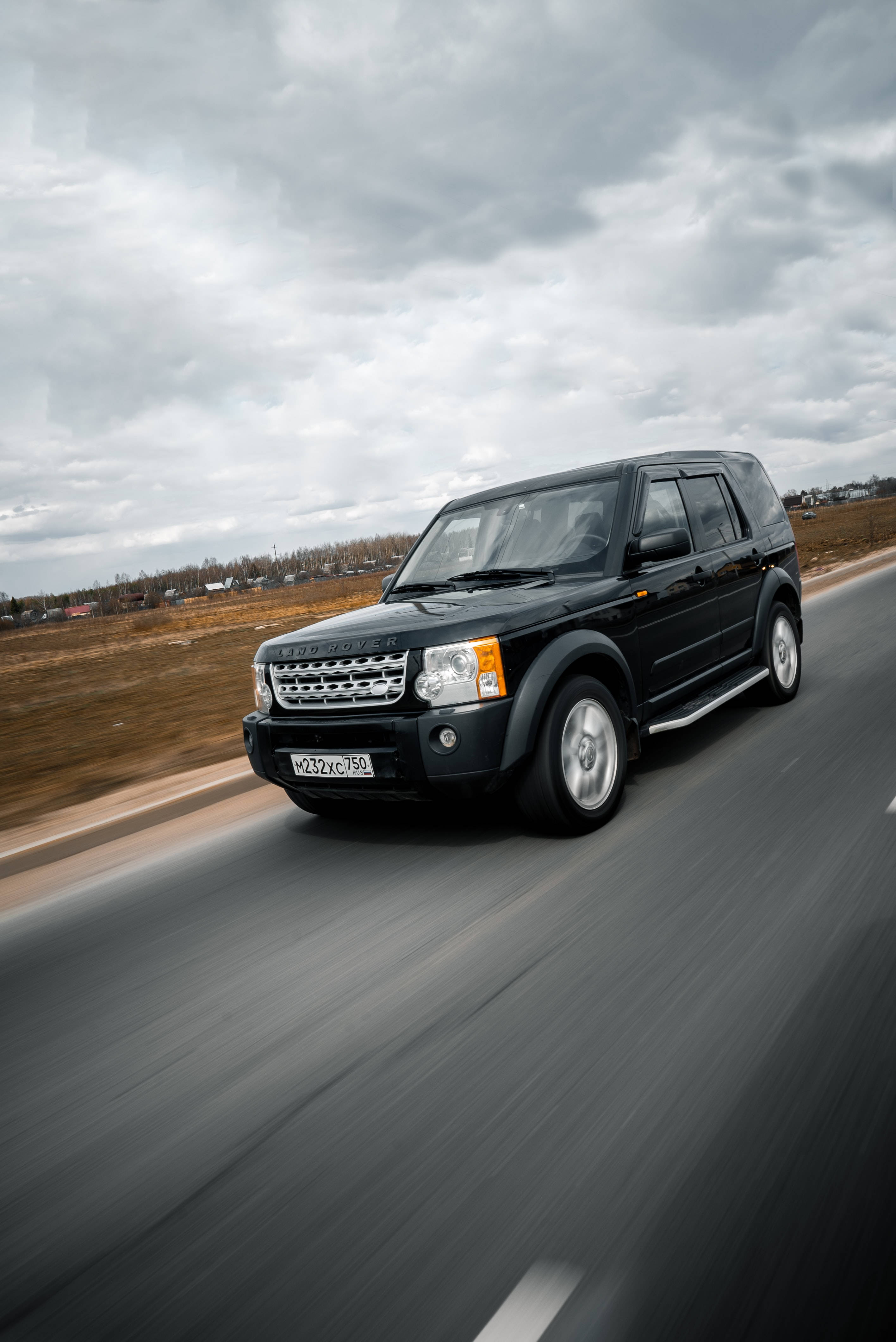 Raven Land Rover Jeep 壁紙 — 一輛黑色 Land Rover Freelander 在陰沉天空下沿鄉村道路疾馳，帶有模糊動態效果。