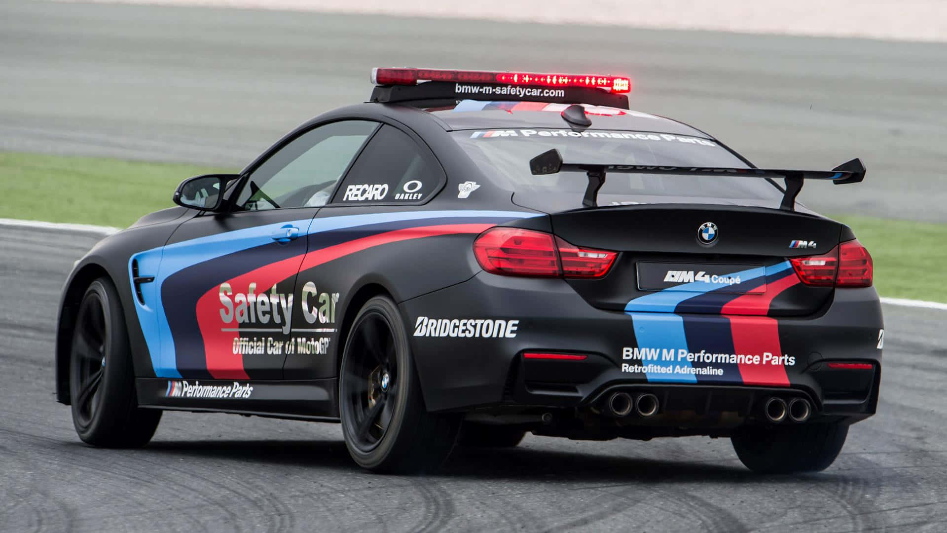 Safety Car 桌布 壁紙 — 一輛黑色BMW M4安全車，帶有紅藍白塗裝，在賽道上疾馳，車頂紅燈閃爍。