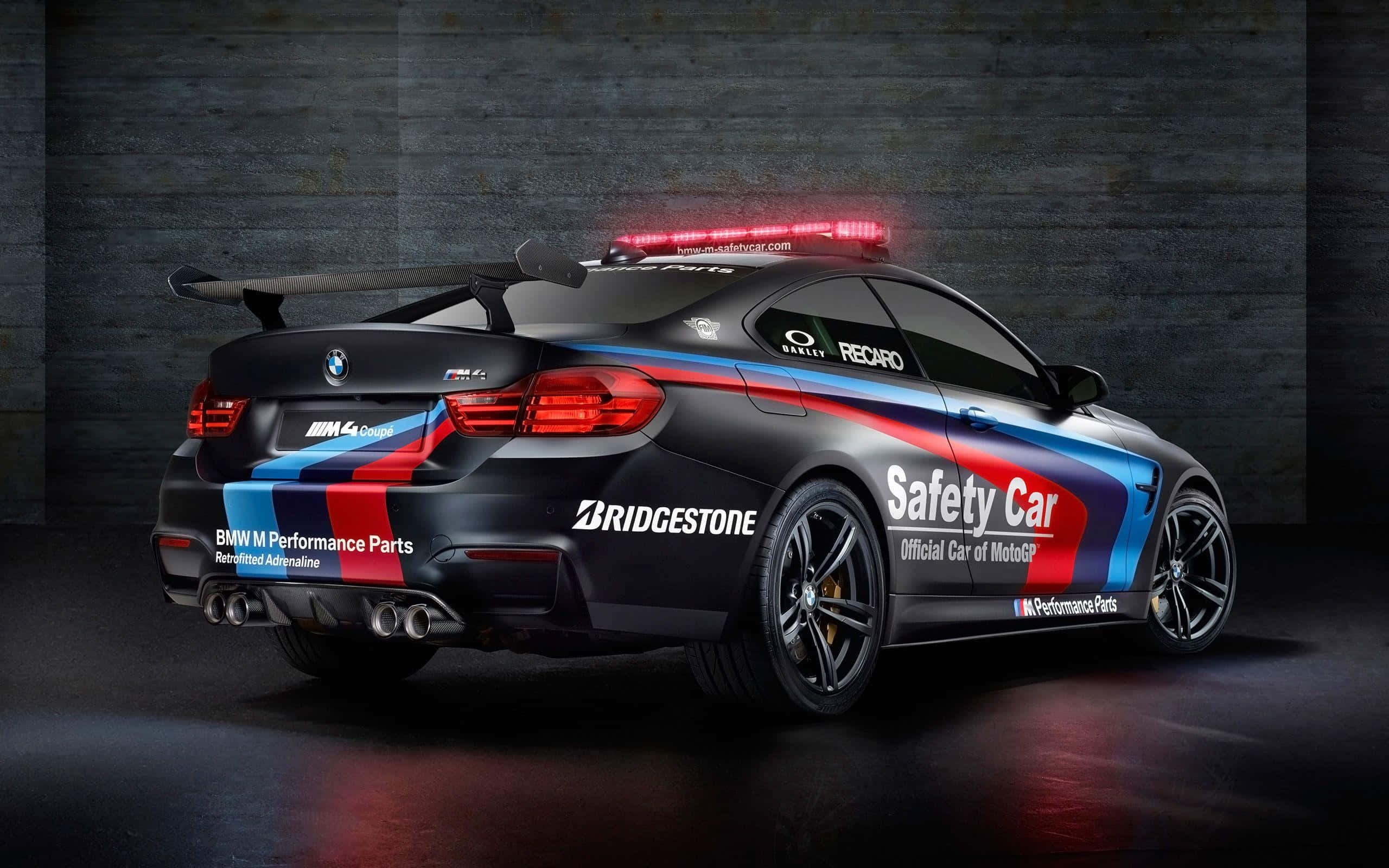 高質素安全戒備車輛圖片 壁紙 — 一輛黑色BMW M4賽車，帶有紅、藍、白色賽車塗裝和閃爍的紅燈，停在深色混凝土車庫地板上。