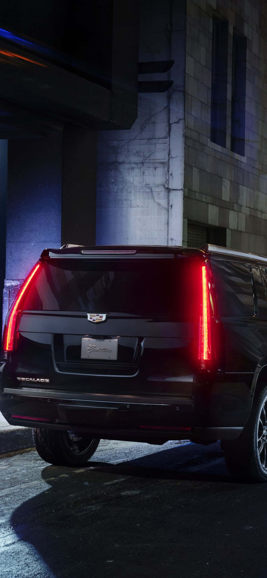 Cadillac Escalade 桌布 壁紙 — 一輛黑色Cadillac Escalade的紅色尾燈照亮了夜晚濕漉漉的城市小巷，背景是混凝土建築。