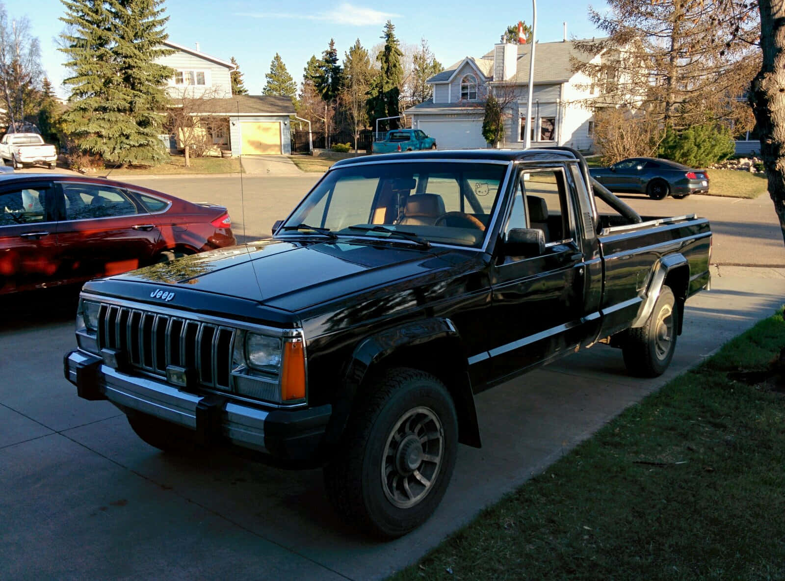 Jeep Comanche 桌布 壁紙 — 一輛黑色Jeep Cherokee皮卡車停在車道上，背景是郊區房屋和樹木，天空晴朗。