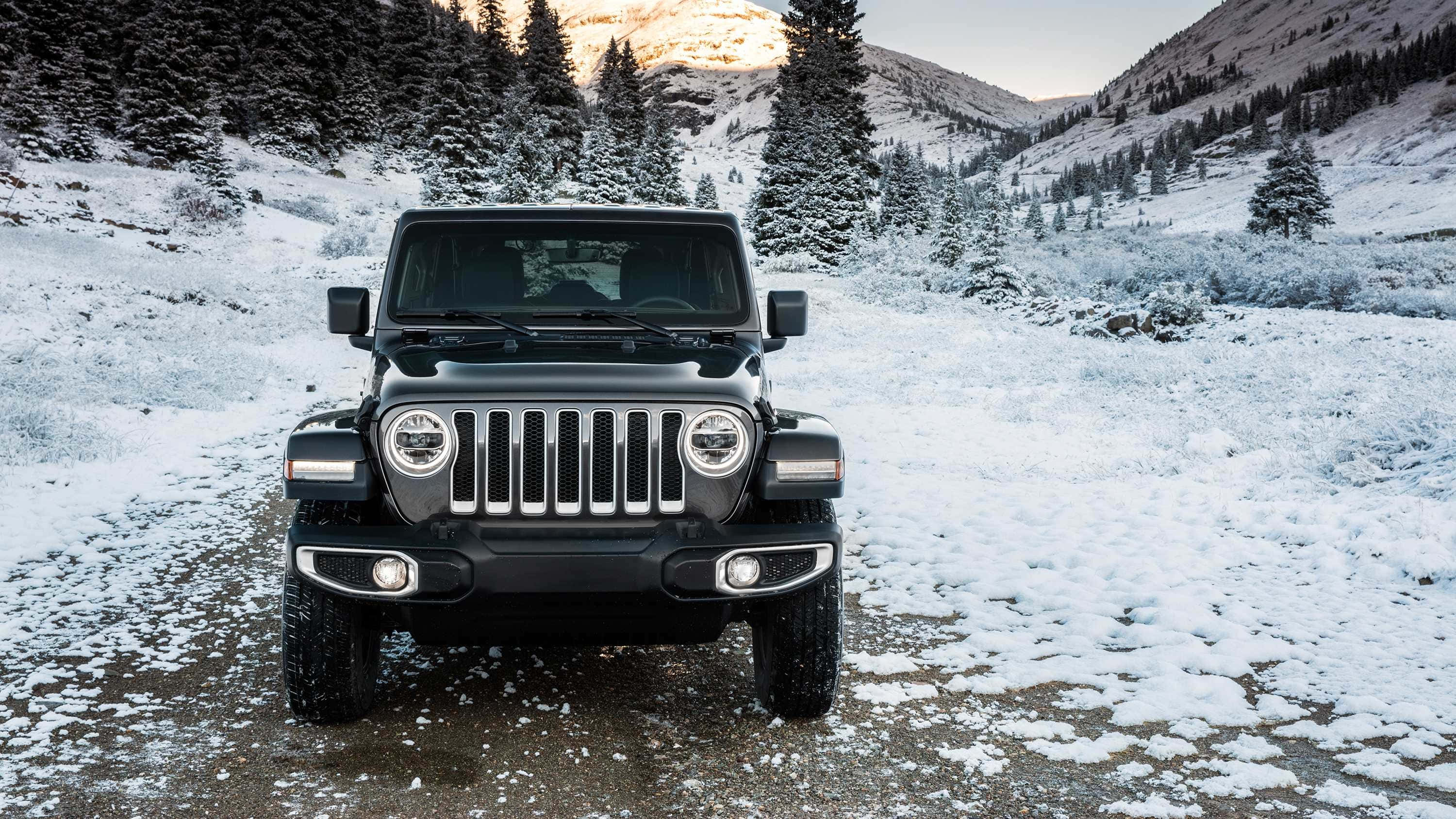 Jeep Patriot 桌布 壁紙 — 一輛黑色Jeep Wrangler大膽地停在白雪覆蓋的山路上，周圍是積雪的常青樹和崎嶇的山峰。