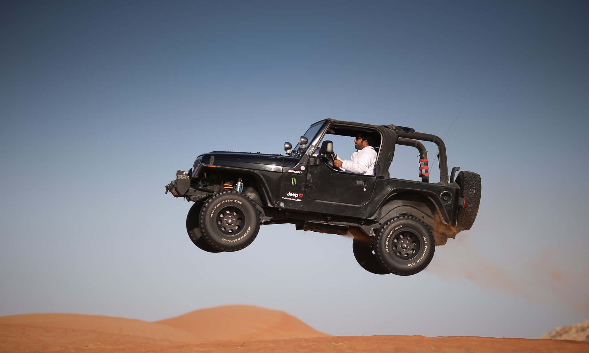 Jeep Cj 桌布 壁紙 — 一輛黑色Jeep Wrangler在清澈藍天下飛越金色沙漠沙丘。