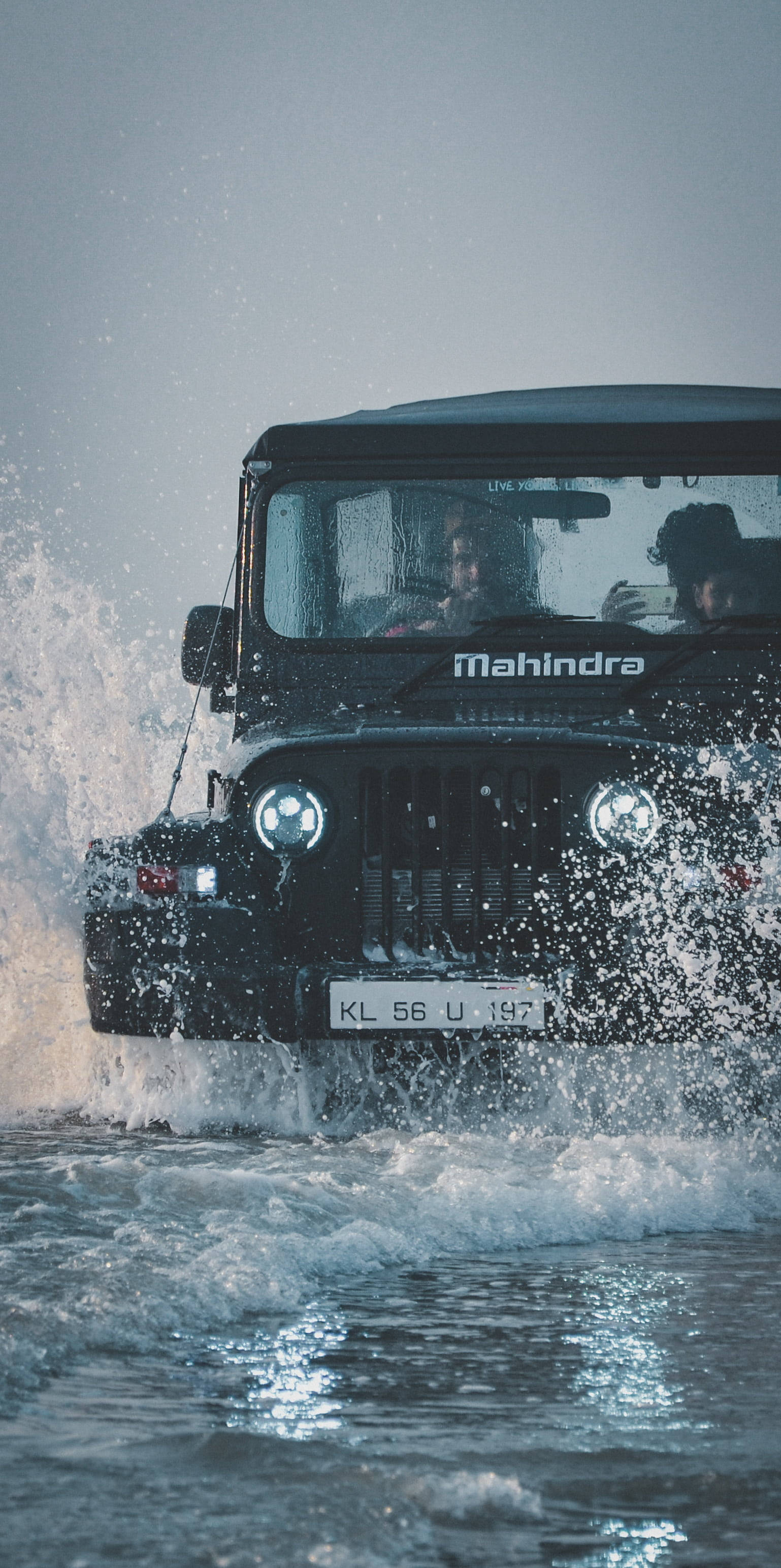 肖像 桌布 壁紙 — 一輛黑色Mahindra吉普車在陰天下行駛過淺水，濺起水花，車內有兩人。