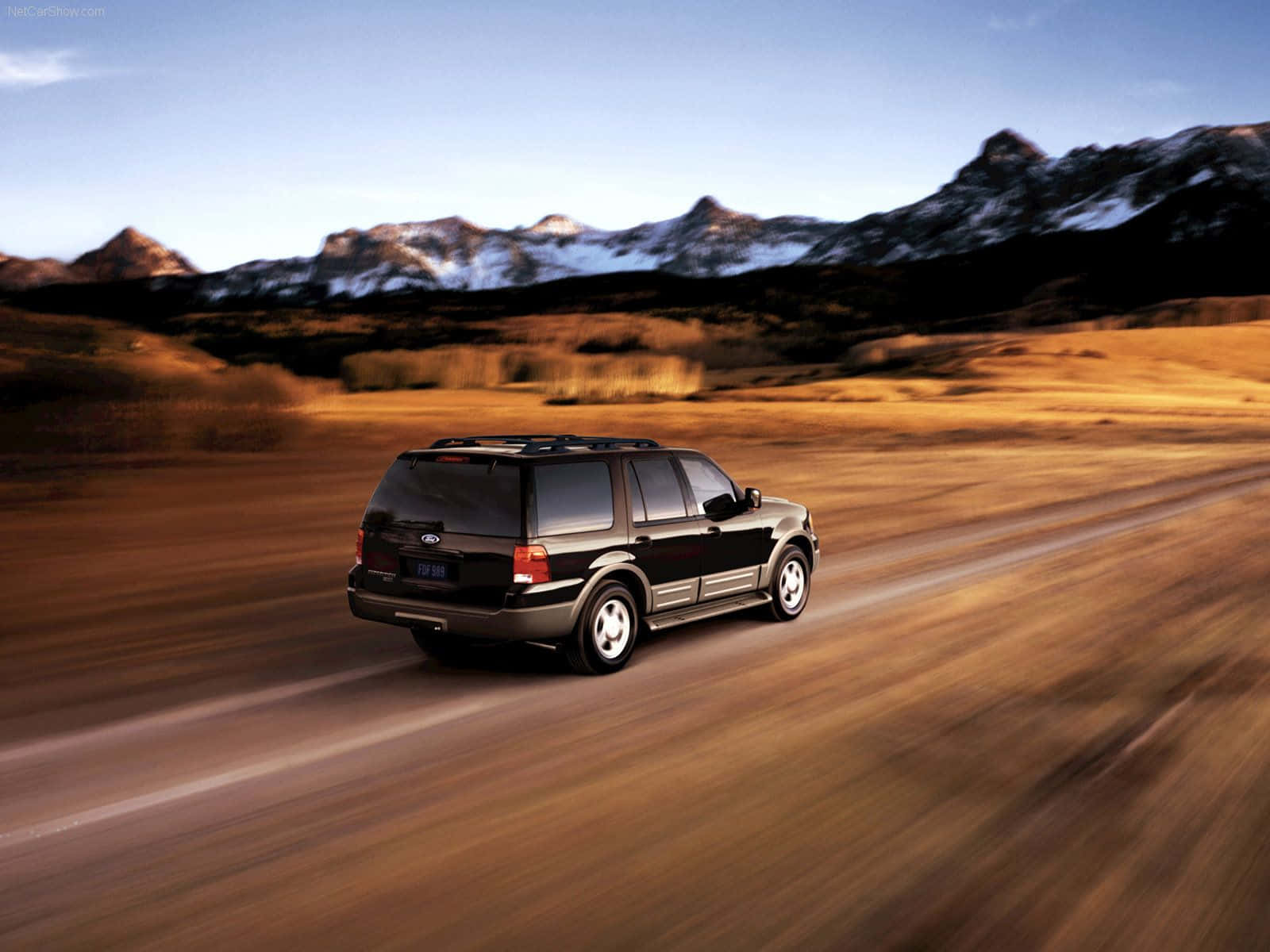 Ford Expedition 桌布 壁紙 — 一輛黑色SUV在沙漠公路上疾馳，背景是白雪覆蓋的山脈，天空晴朗。