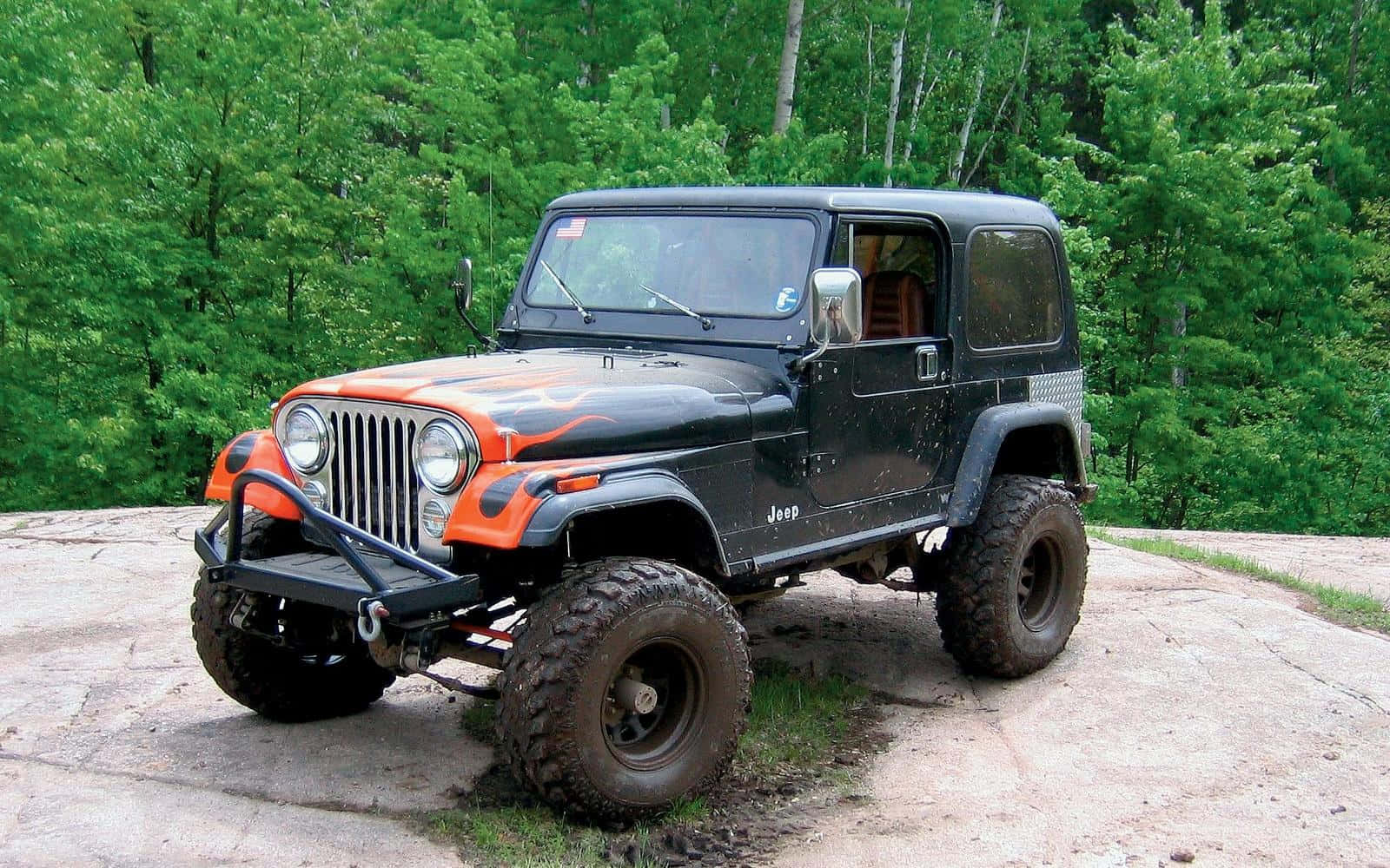 Jeep Cj 桌布 壁紙 — 一輛黑色和橙色的Jeep Wrangler配備大型輪胎，停泊在岩石露頭上，周圍是茂密的綠色森林。