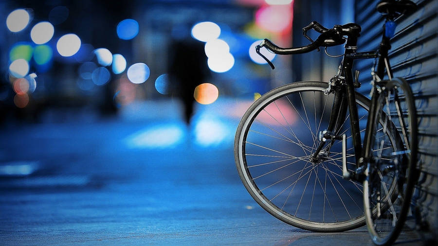 桌布 壁紙 — 一輛黑色單車在潮濕的城市街道上靠著金屬百葉窗，背景有發光的散景燈光。