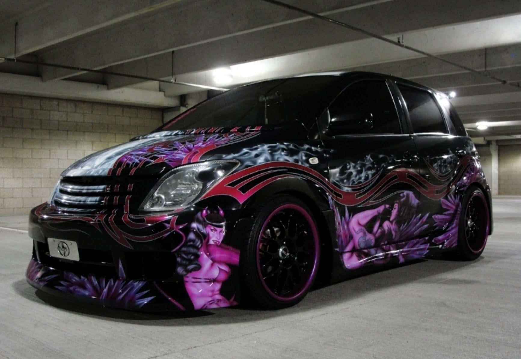 Modified Car 桌布 壁紙 — 一輛黑色定制汽車，帶有充滿活力的紫色和粉紅色惡魔主題塗鴉藝術，停在混凝土地下車庫中。
