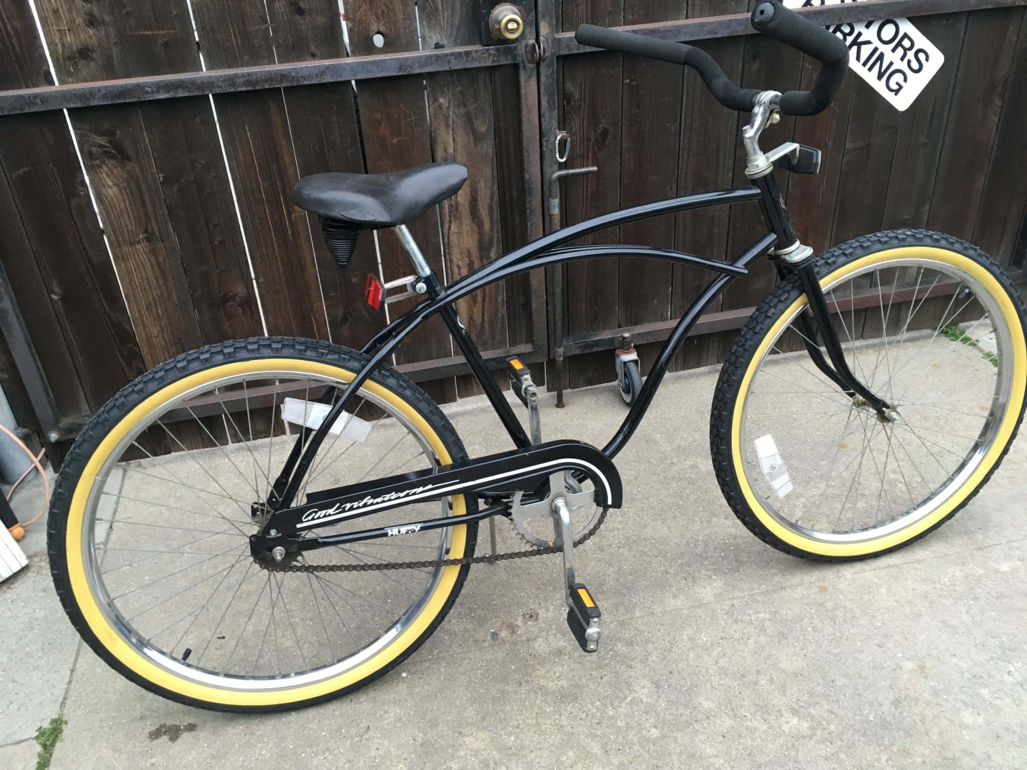 Beach Cruiser 桌布 壁紙 — 一輛黑色巡航自行車配亮黃色輪胎，靠在混凝土庭院中經風化的木柵欄上。