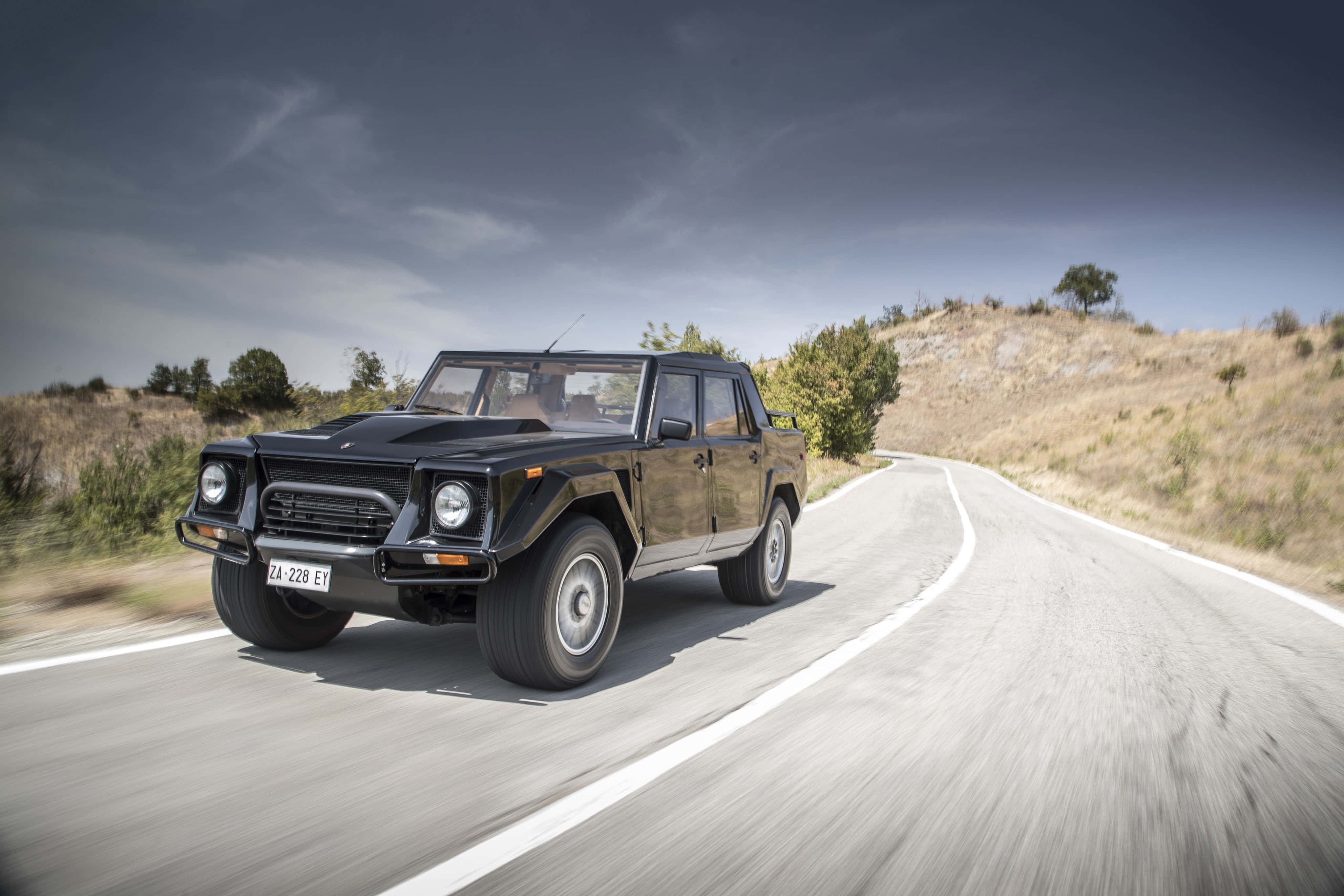 Lamborghini Lm002 桌布 壁紙 — 一輛黑色林寶堅尼LM002 SUV在陰天下沿著蜿蜒的鄉村道路飛馳。