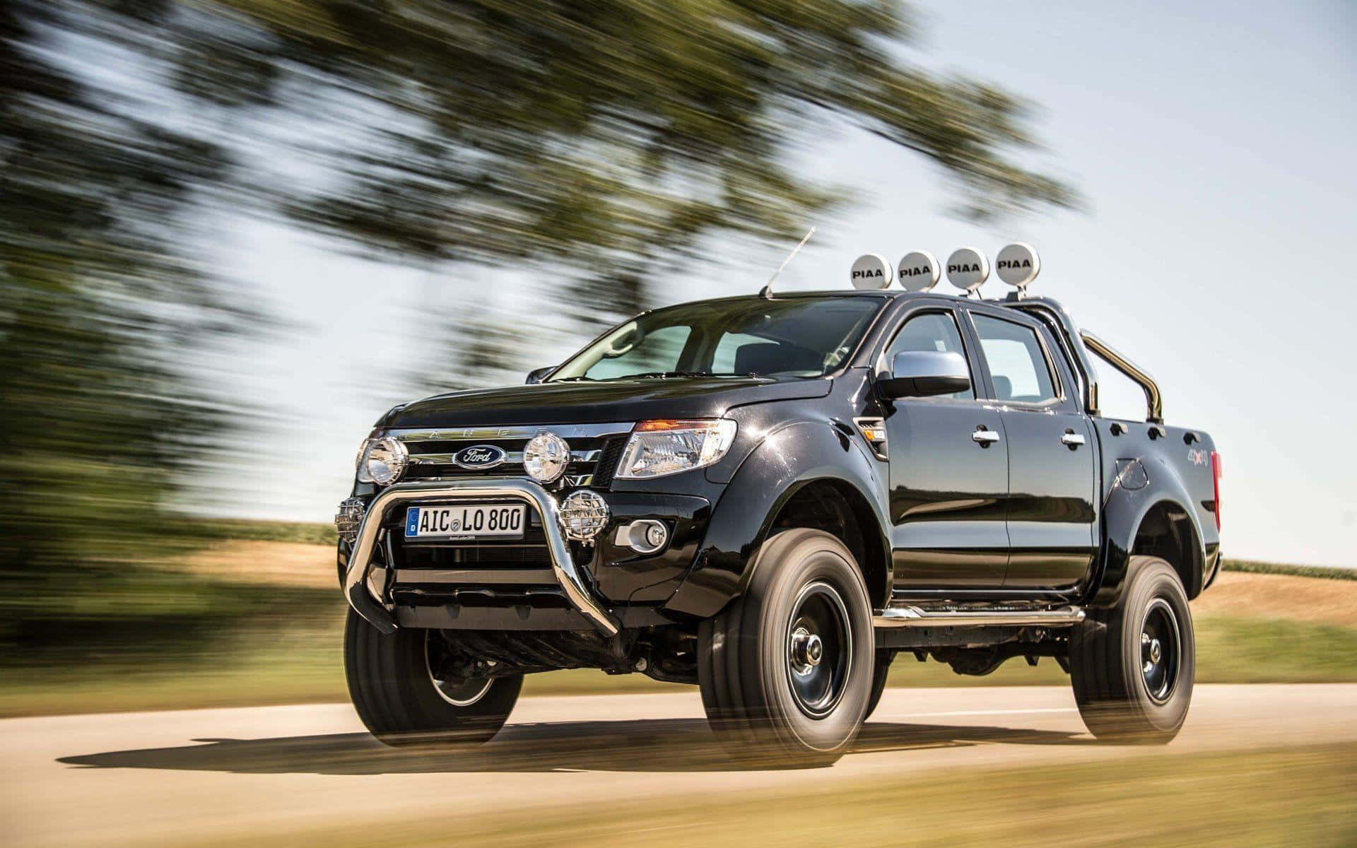 Ford Ranger 桌布 壁紙 — 一輛黑色福特 Ranger 皮卡車在鄉間道路上疾馳，背景是模糊的綠樹和金黃色的田野。