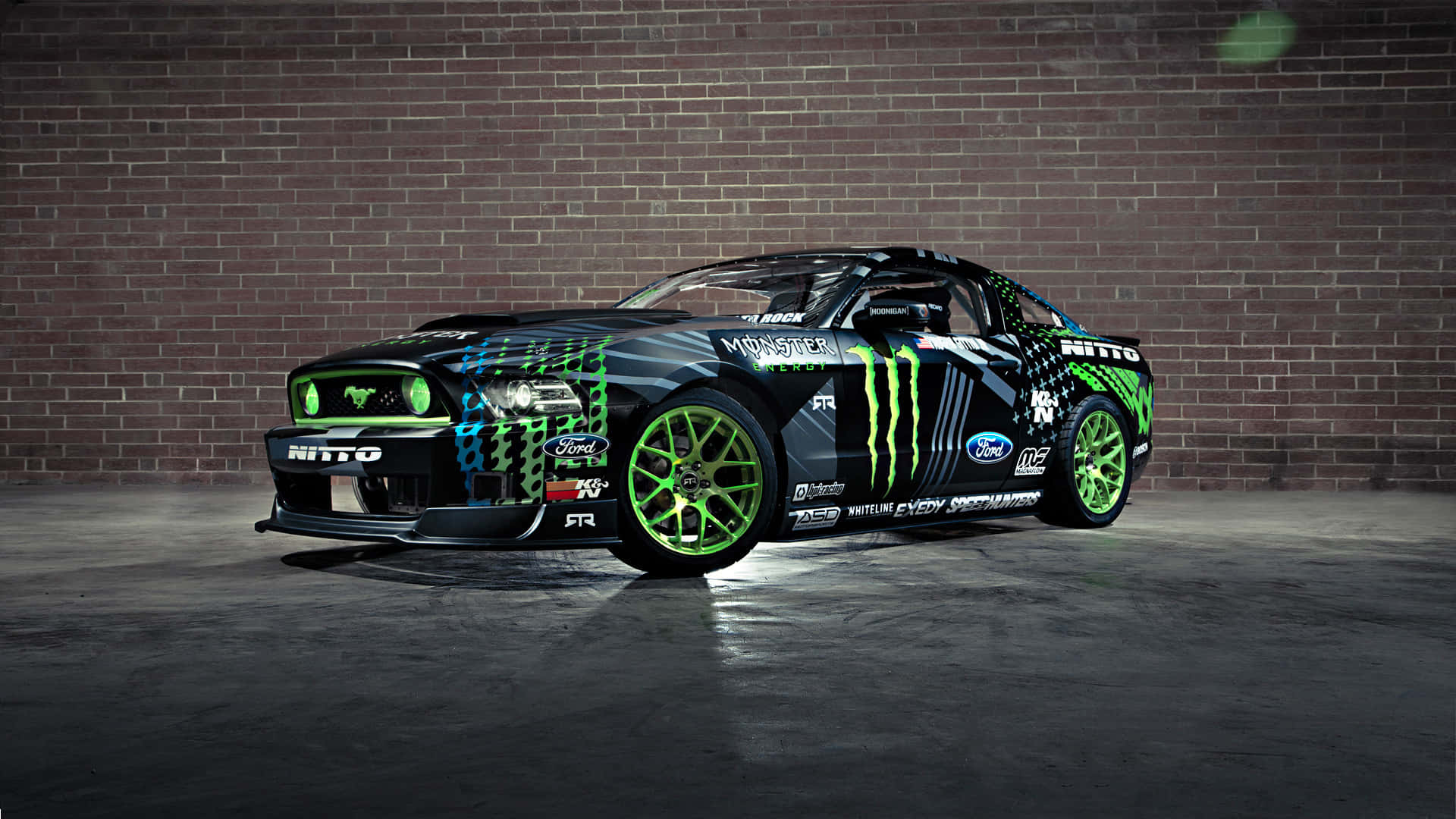 Monster Energy 桌布 壁紙 — 一輛黑色福特野馬貼有螢光綠色Monster Energy貼紙，停在光線昏暗的車庫中，靠著磚牆。