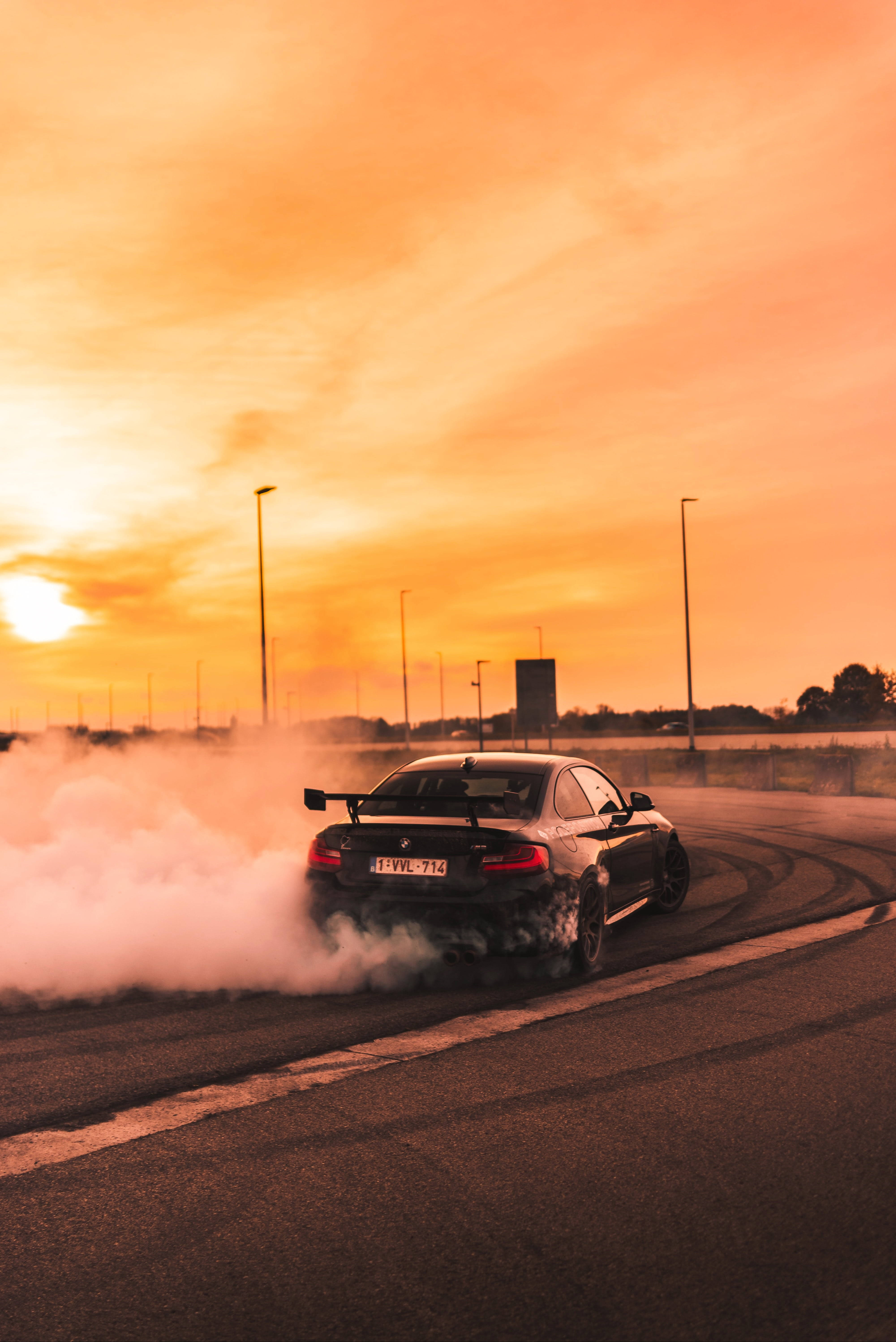 speeding car 桌布 壁紙 — 一輛黑色跑車在空蕩蕩的道路上，於夕陽下火紅橙色的天空中，伴隨著煙霧飄移。