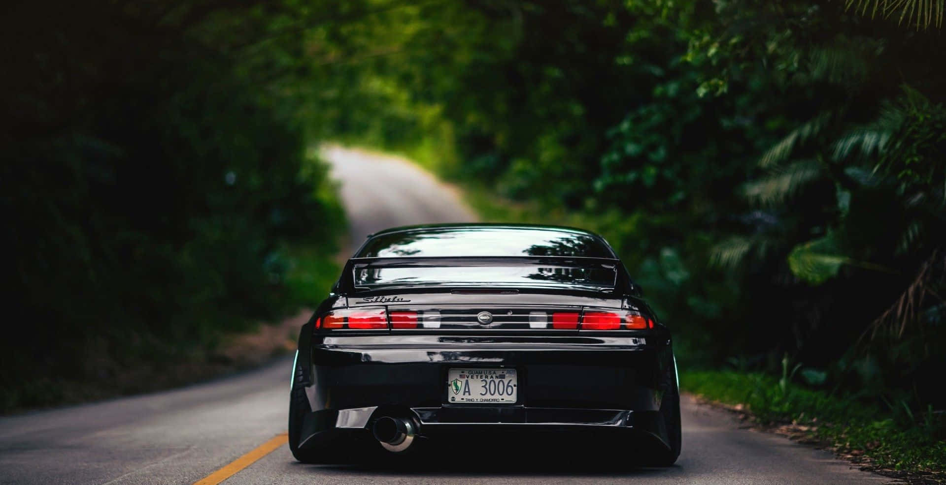 JDM 車 桌布 壁紙 — 一輛黑色跑車沿著蜿蜒的森林道路行駛，周圍是茂密的綠樹。