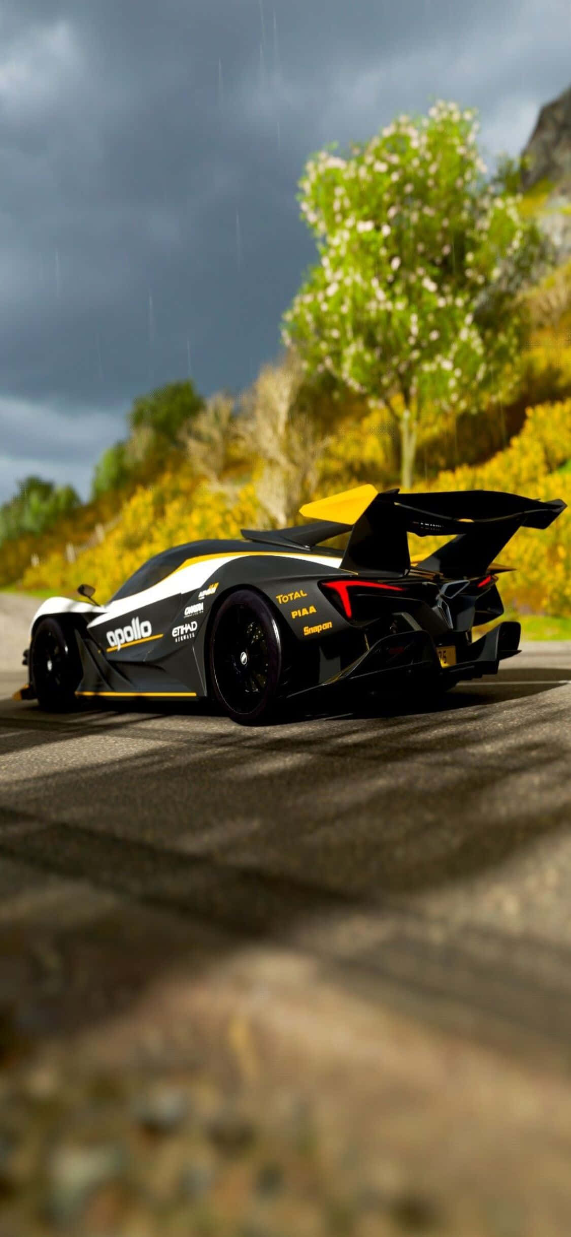 一輛黑黃相間的車在道路上駕駛 壁紙 — 一輛黑黃色的阿波羅 Intensa Emozione 超級跑車在暴風雨的天空下，沿著濕滑的山路疾馳，周圍是鮮豔的秋葉。