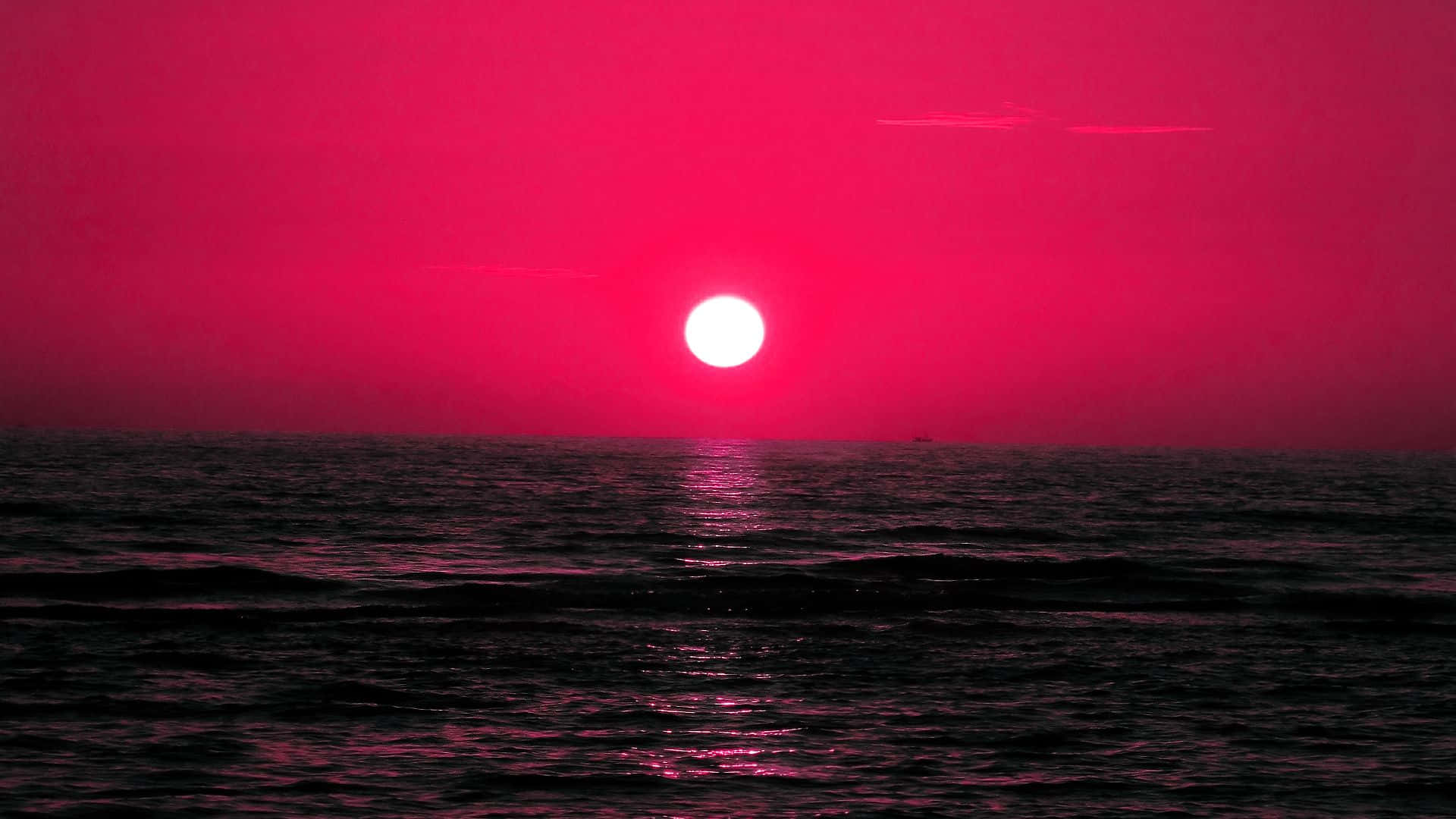 Red Sunset 桌布 壁紙 — 一輪充滿活力的粉紅色太陽在黑暗的海洋上落下，在漣漪的水面上投射出發光的倒影。