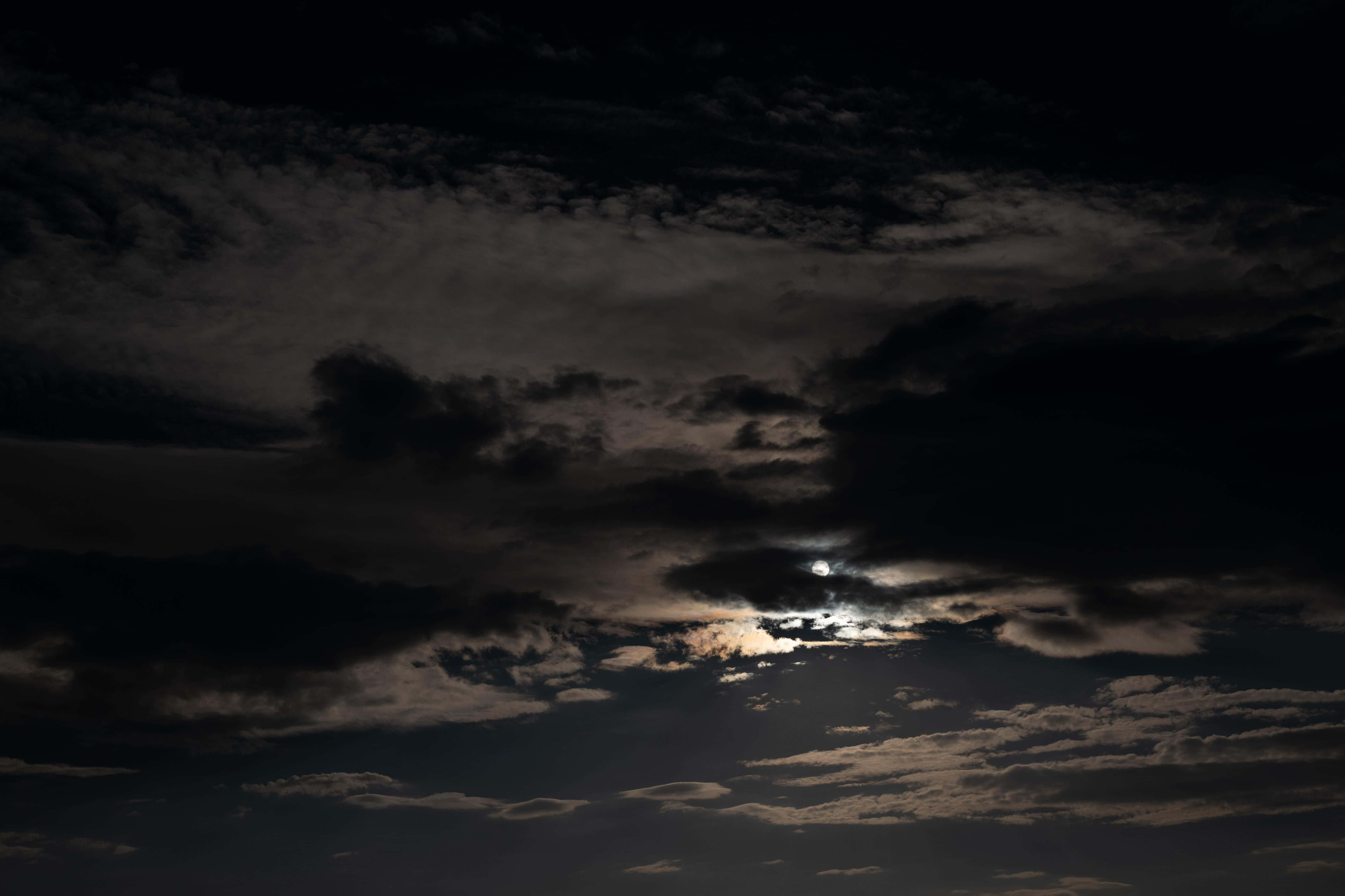 Dark Sky 桌布 壁紙 — 一輪明亮的月亮穿透戲劇性的烏雲，在充滿氛圍的夜空中。